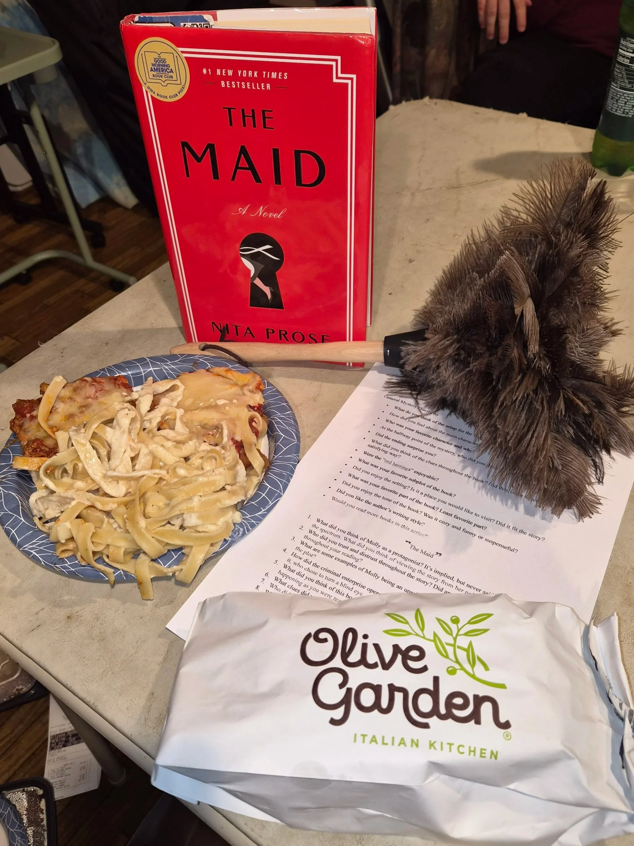 The book "The Maid" next to takeout food from the Olive Garden.