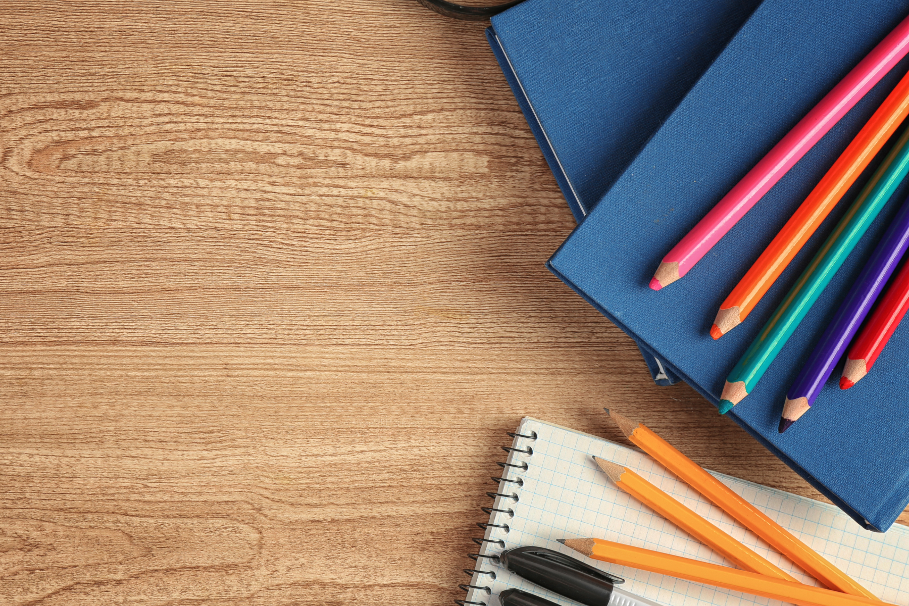 Blue notebooks, colored pencils, a spiral notebook, and a black marker on a wooden surface.