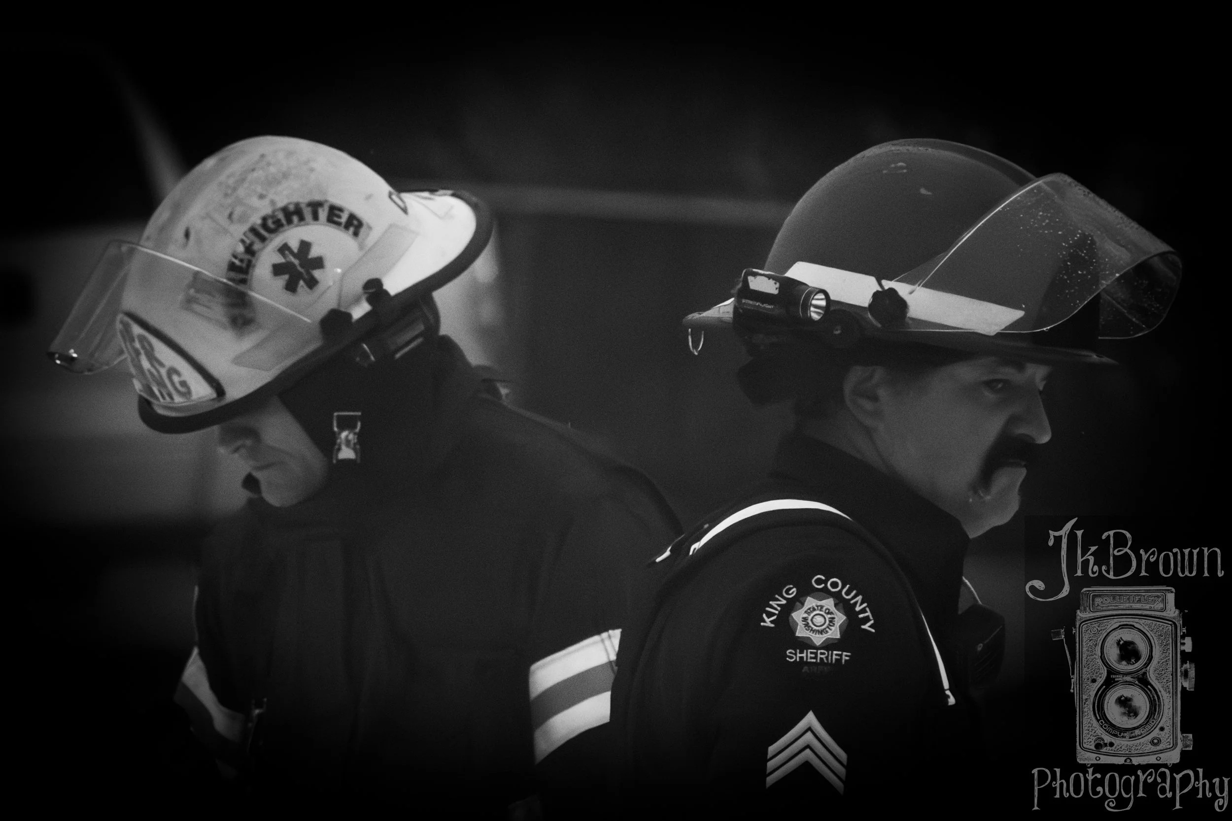 Black and white photo of two police officers in uniform wearing helmets with visors, standing back to back, with the badge and text 'King County Sheriff' visible on the right officer's uniform.