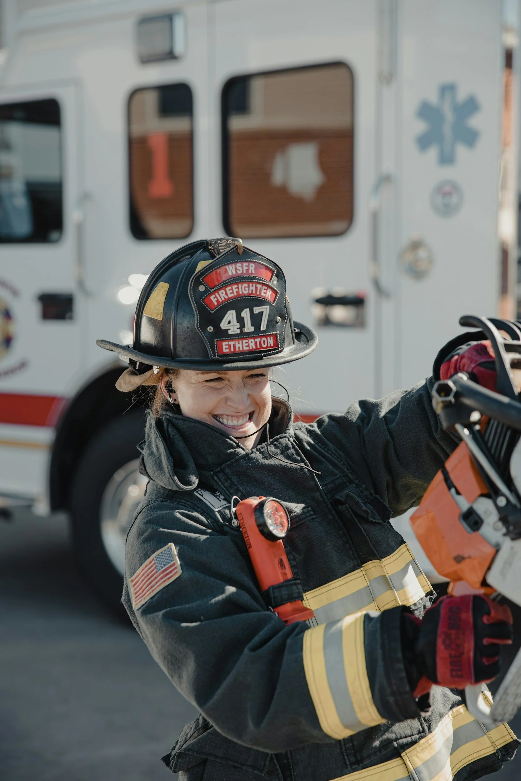 Firefighter smiling in front of a fire truck, wearing a helmet labeled ETherton and WSFR.
