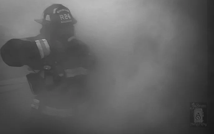 Firefighter in full gear amid smoke, inspecting a scene.