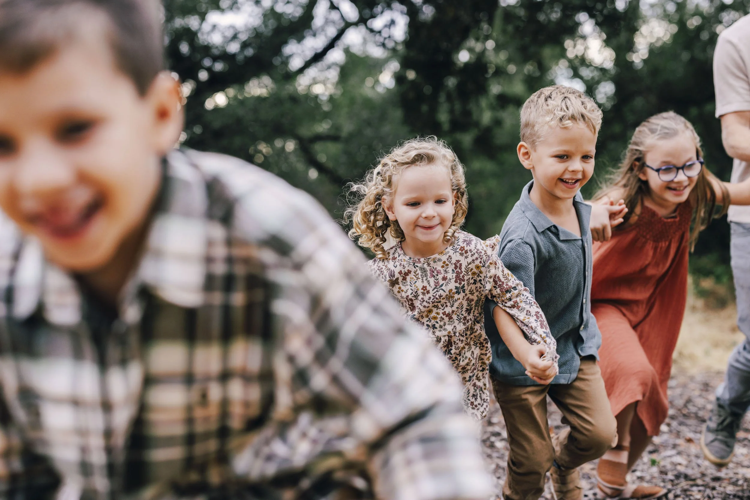 Children holding hands and playing outdoors in a grassy area with trees in the background