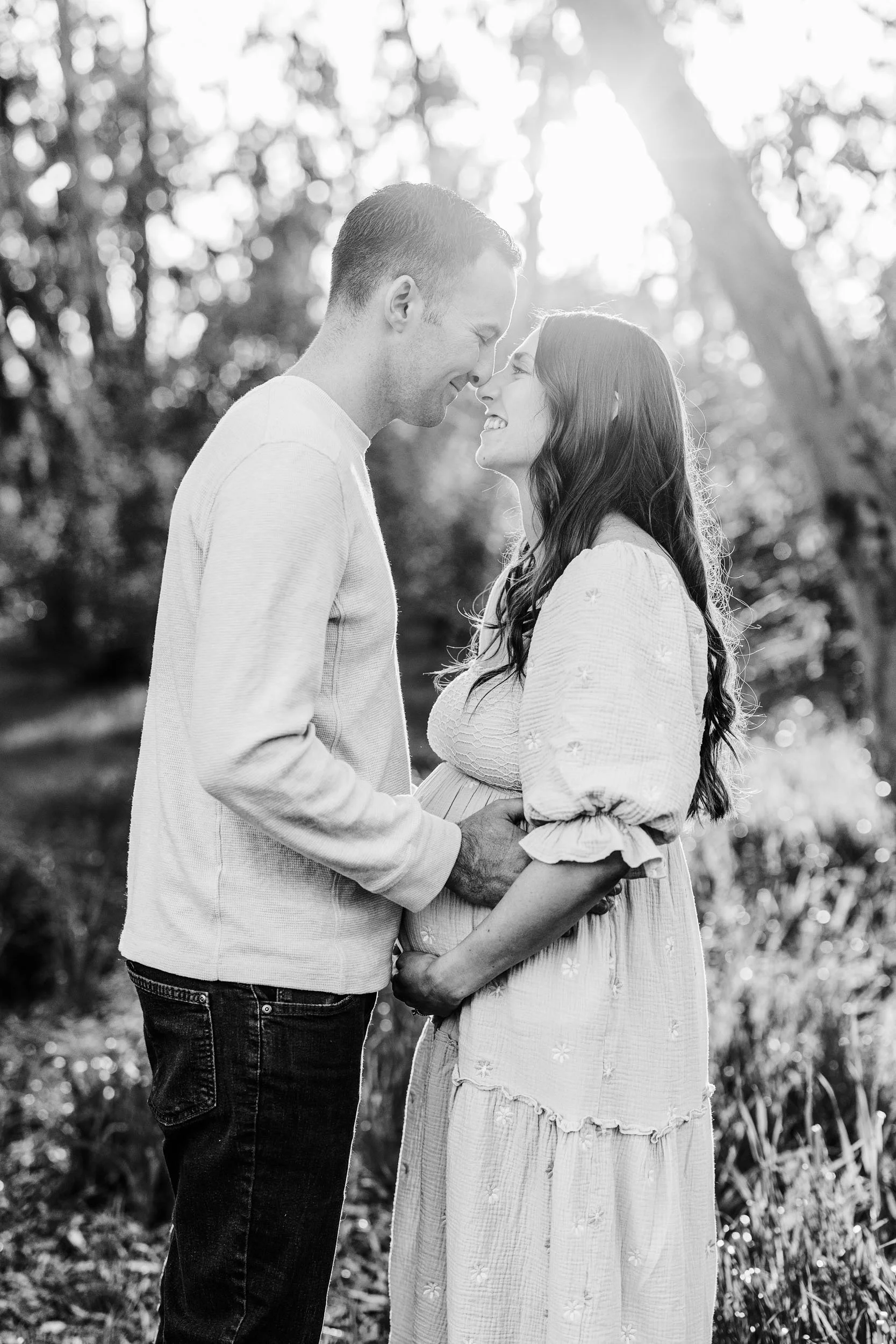 A man and woman face each other and embrace a pregnant belly during their maternity photo session in Sacramento