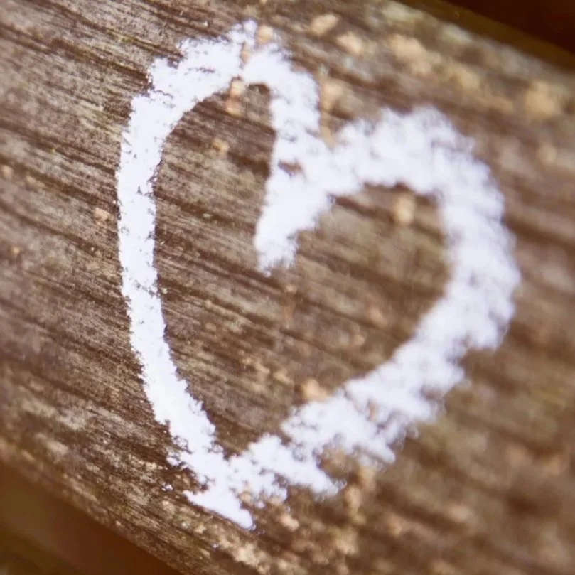 Close-up of a wooden surface with a heart shape drawn in white chalk or powder.
