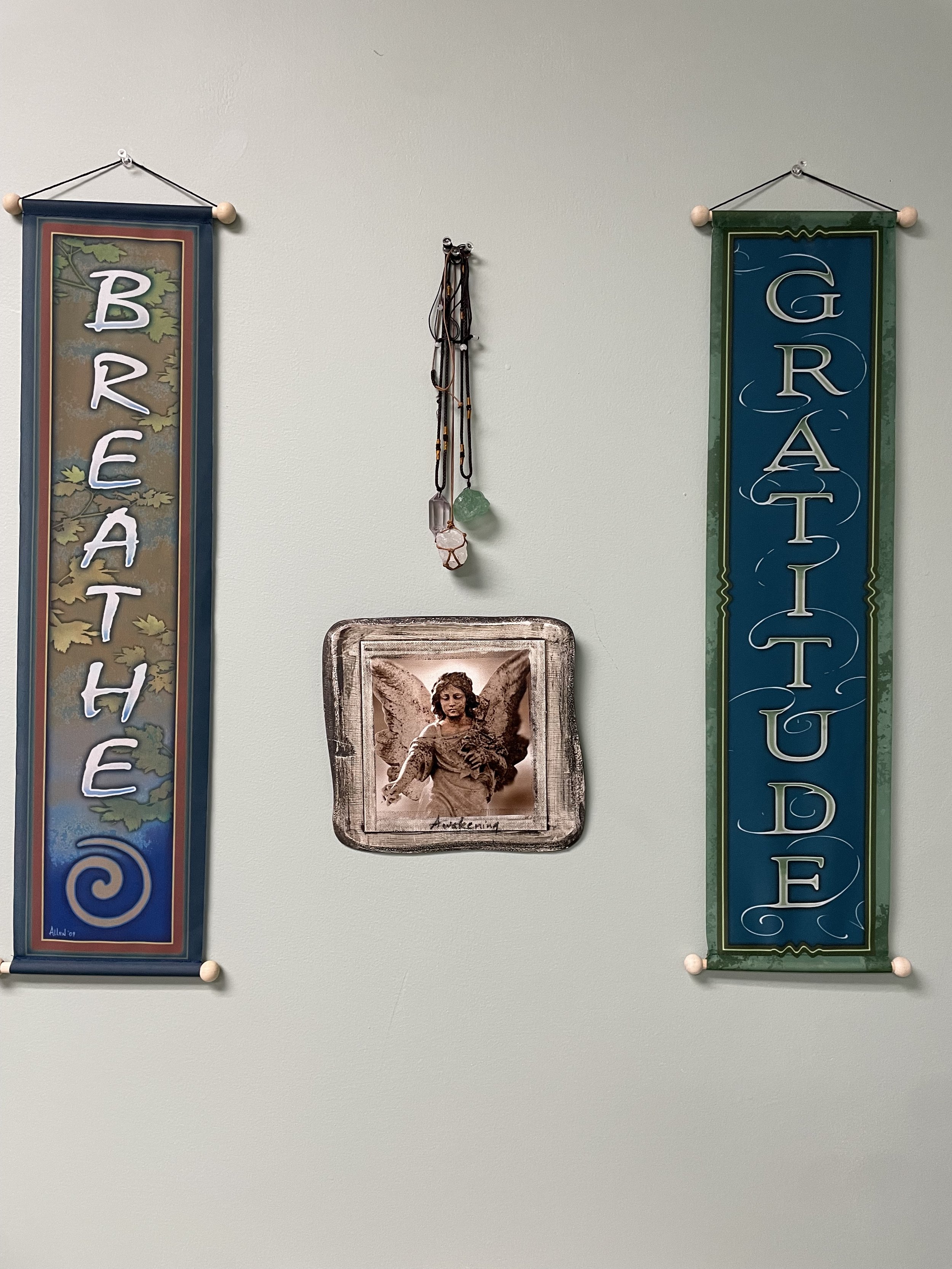 Wall decor with 'Breathe' and 'Gratitude' banners, angel picture, and hanging crystals.