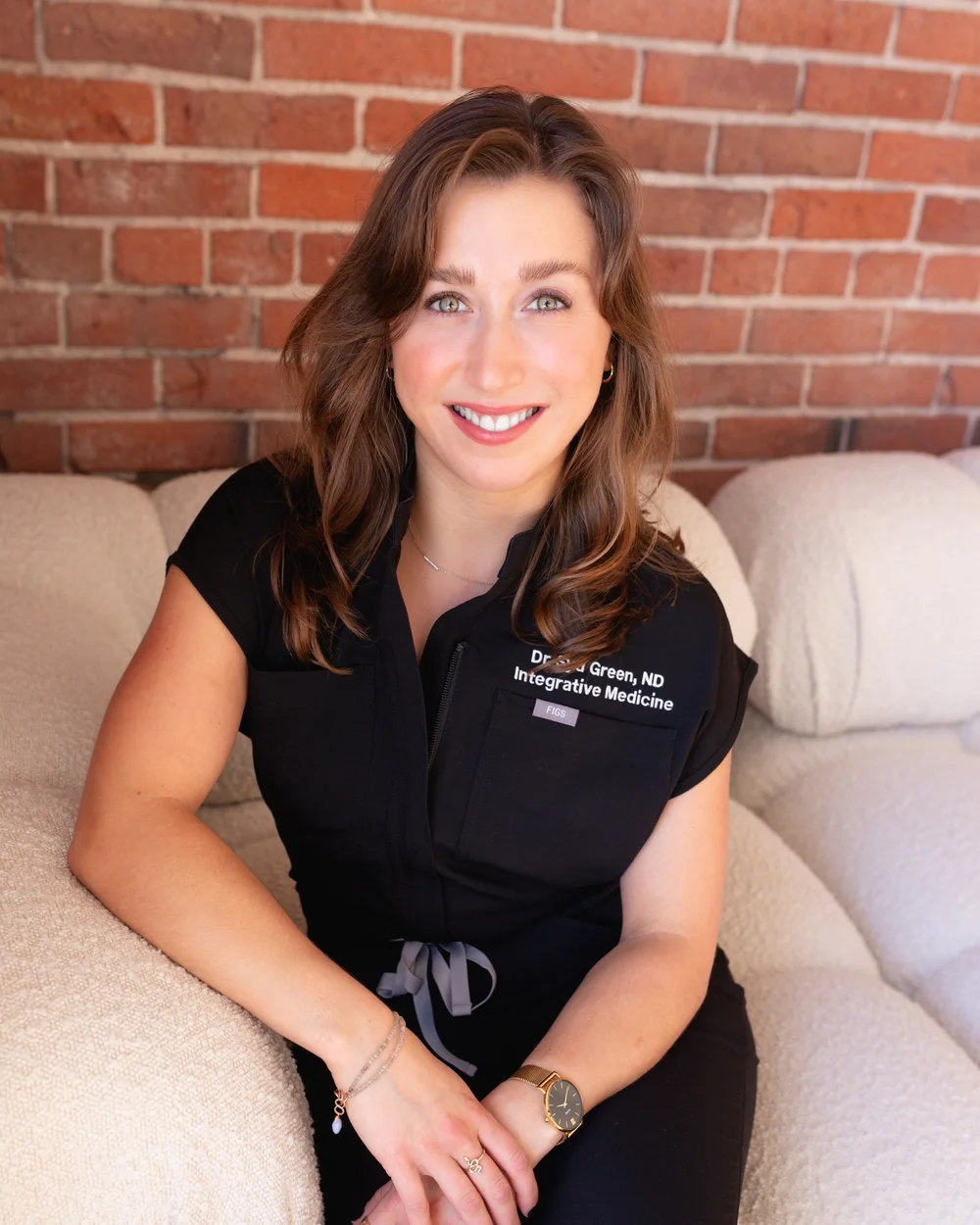 Dr. Sydney Green, ND, naturopathic doctor in Victoria, BC, in black scrubs against a brick wall.