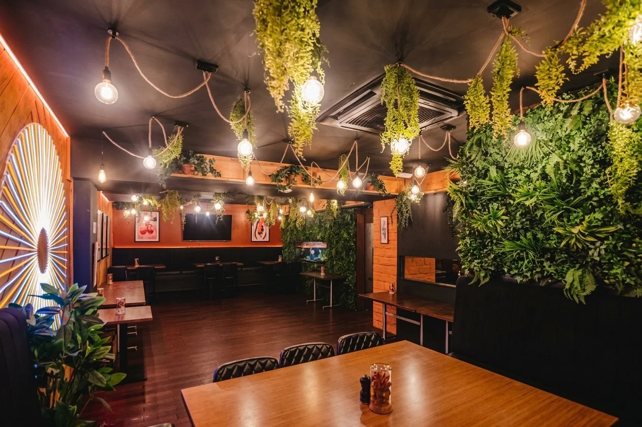 Interior of a cozy restaurant or cafe with hanging lights, greenery, and wooden decor.