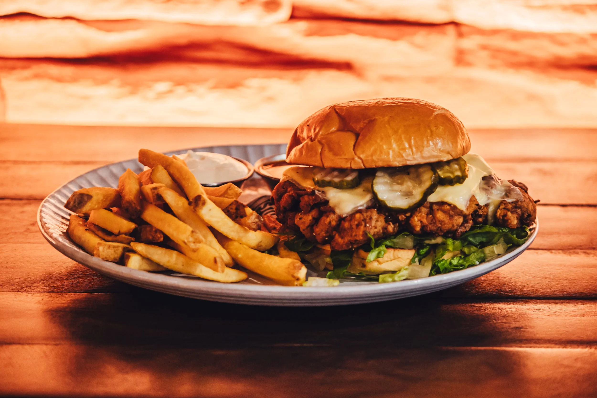 Plate with French fries and a cheeseburger with pickles, lettuce, cheese, and a brioche bun on a wooden table.
