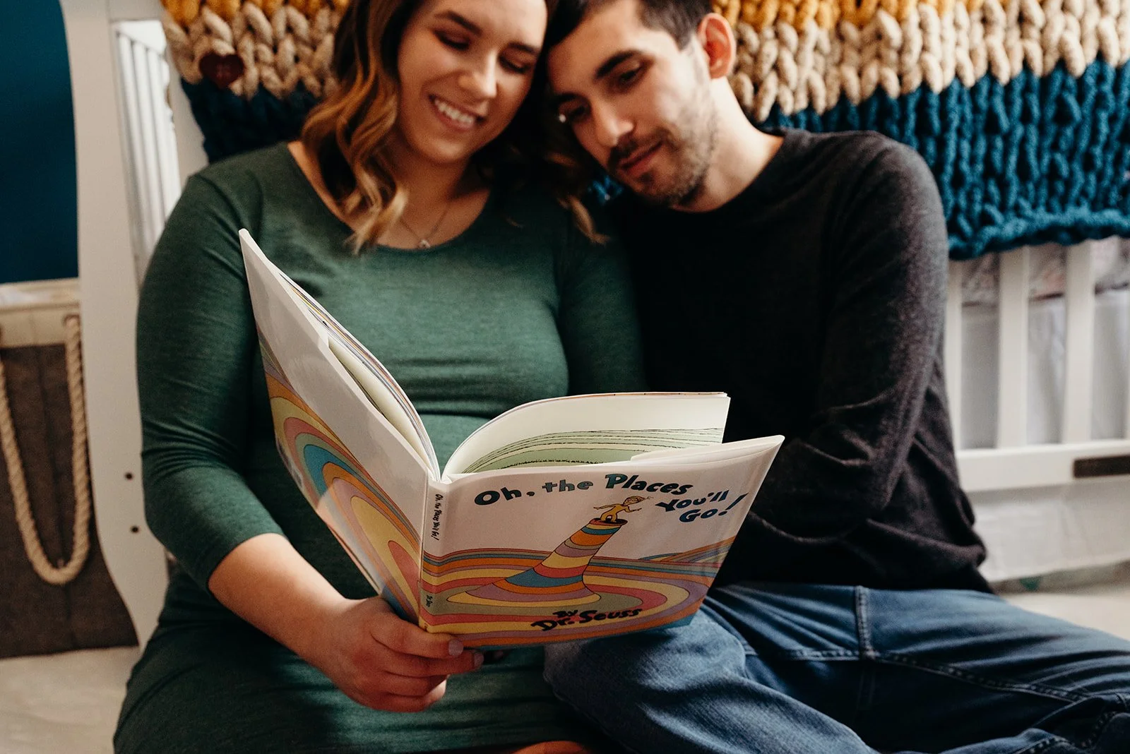 A woman and man sitting close together, reading a colorful book titled "Oh, the Places You'll Go!" by Dr. Seuss, in a cozy home setting.