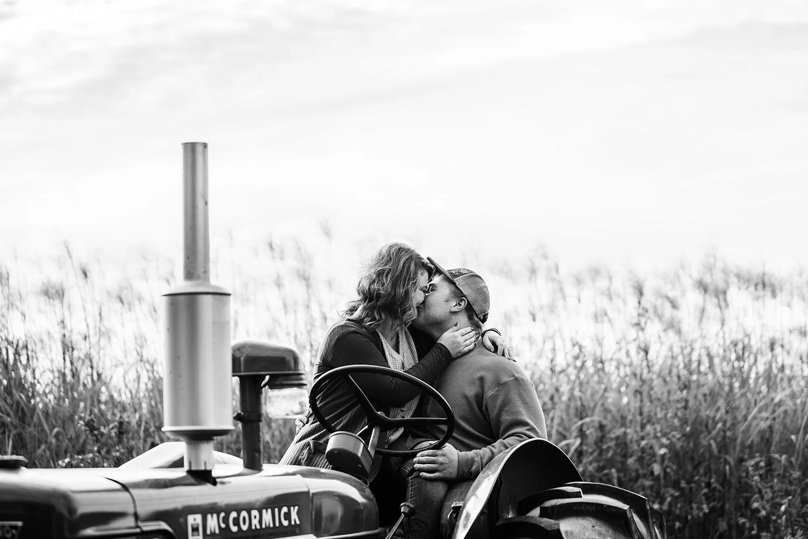 A couple shares a kiss while sitting on a tractor in a field.