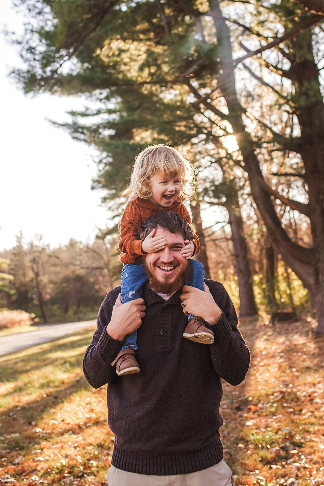 A man carrying a young girl on his shoulders in a park during autumn, both smiling and enjoying the moment.