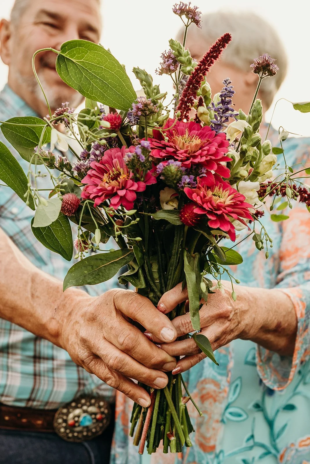 A man and woman holding a colorful bouquet of flowers.