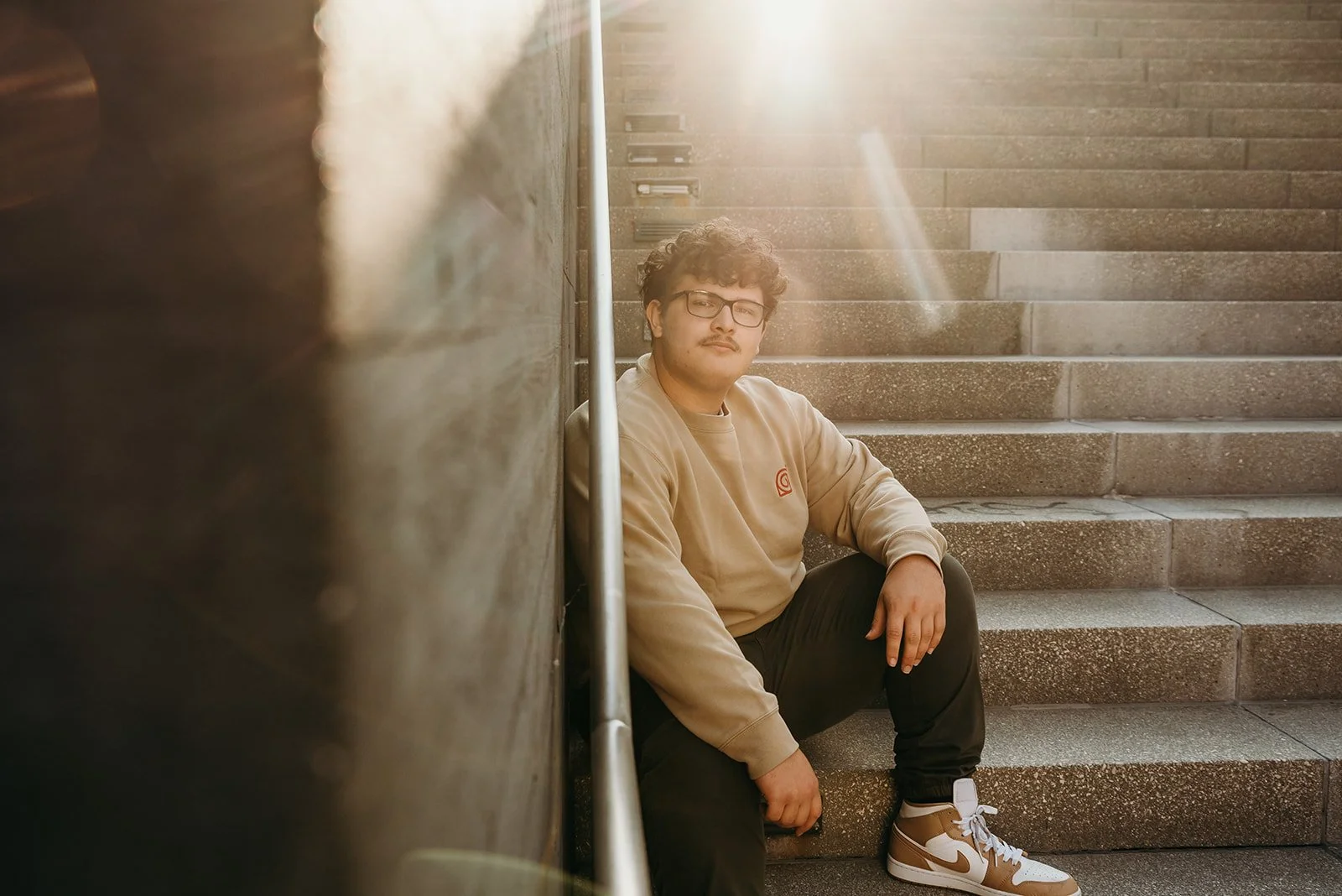 A young man sitting on a concrete staircase, leaning against a wall, with sunlight shining behind him.