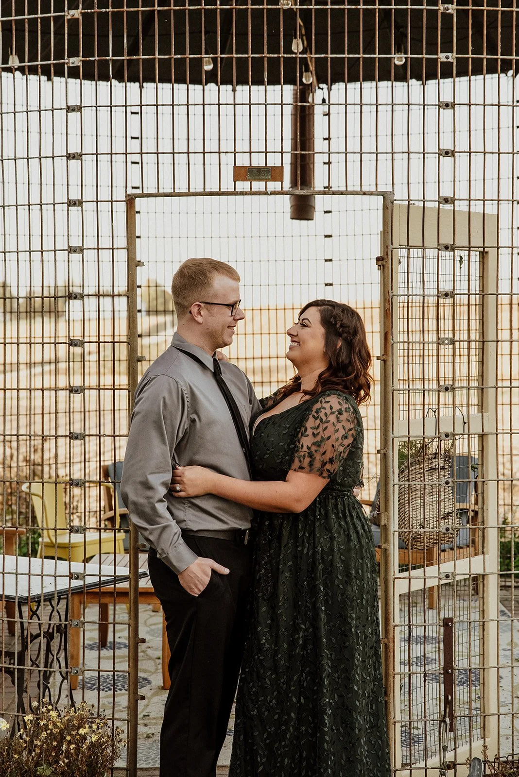 A man and woman smiling at each other inside a metal cage-like structure outdoors during sunset.