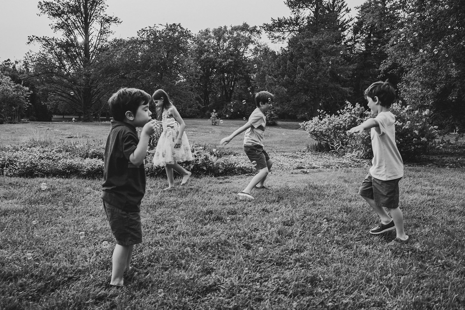 Four children playing with bubbles in a park on a cloudy day.