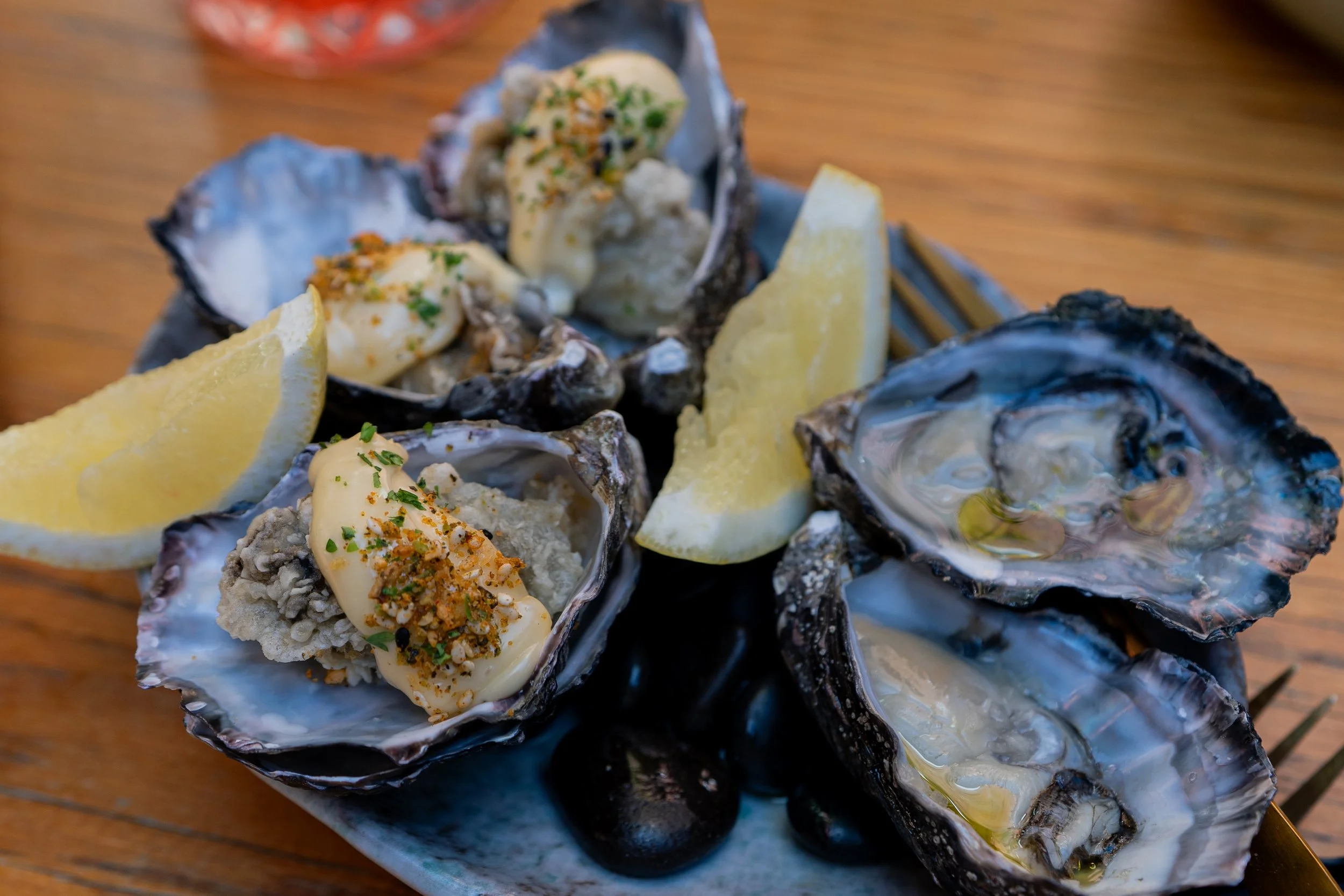 Close-up of fresh oysters on a plate with lemon wedges, garnished with herbs and spices, on a wooden table.
