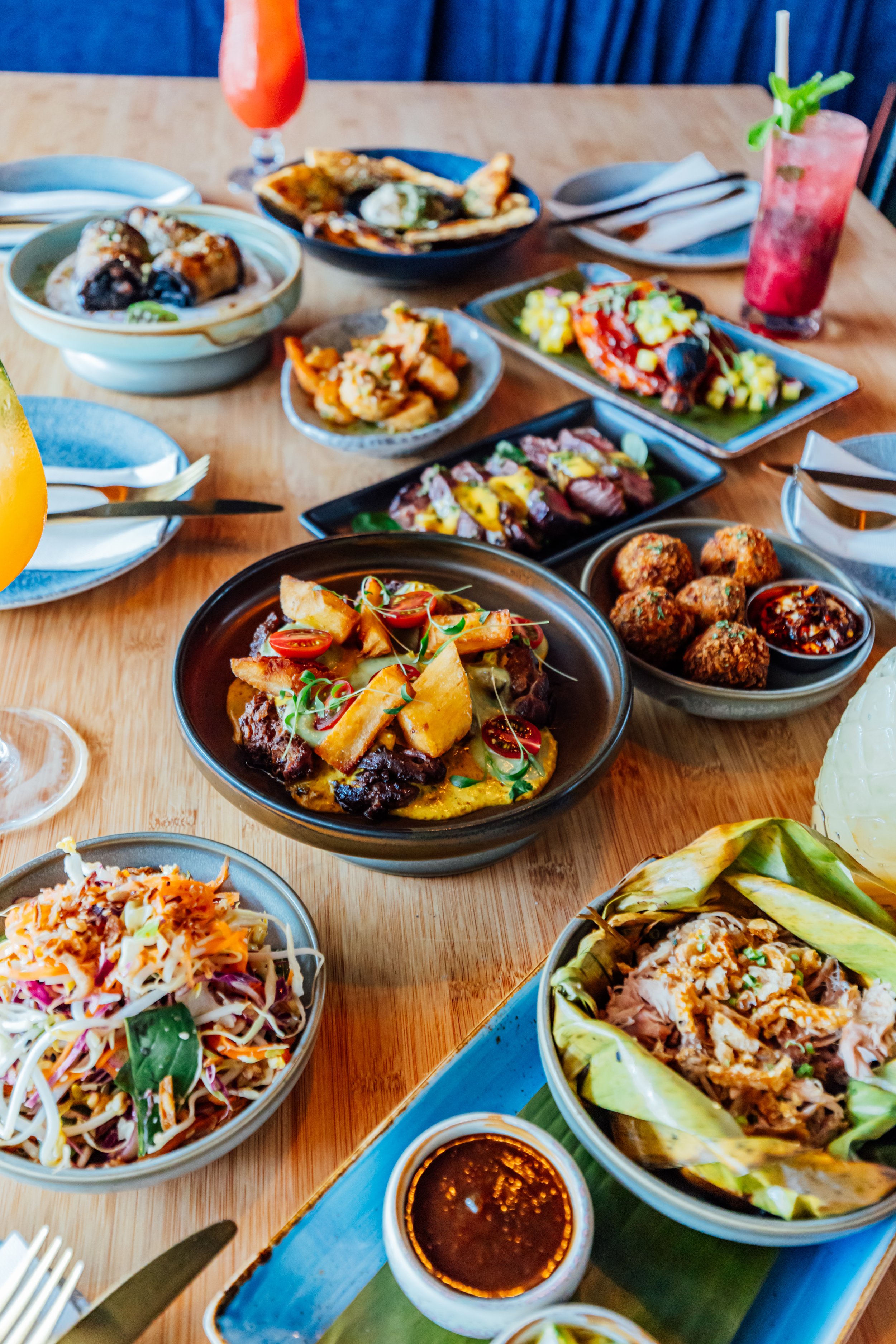 Table filled with various Pacific dishes including Kalua Pork, Slaw, Sirloin, Lamb, Prawns and Flat Bread