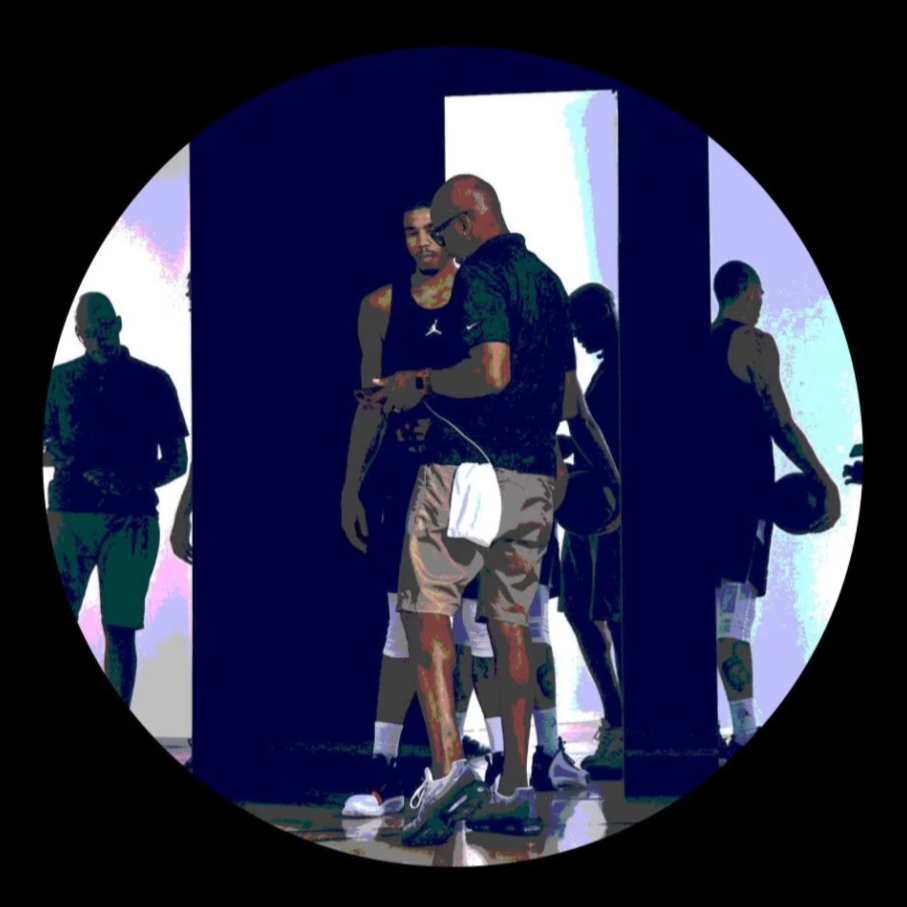 Young men in athletic clothing, some holding basketballs, in a room with a doorway, seen through a circular frame.