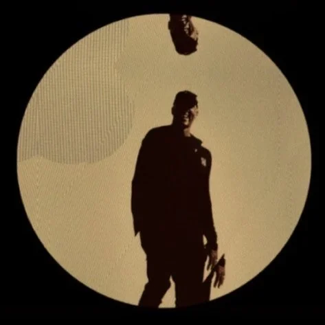 Silhouette of a person holding a microphone, projected on a large circular screen during a presentation or performance.