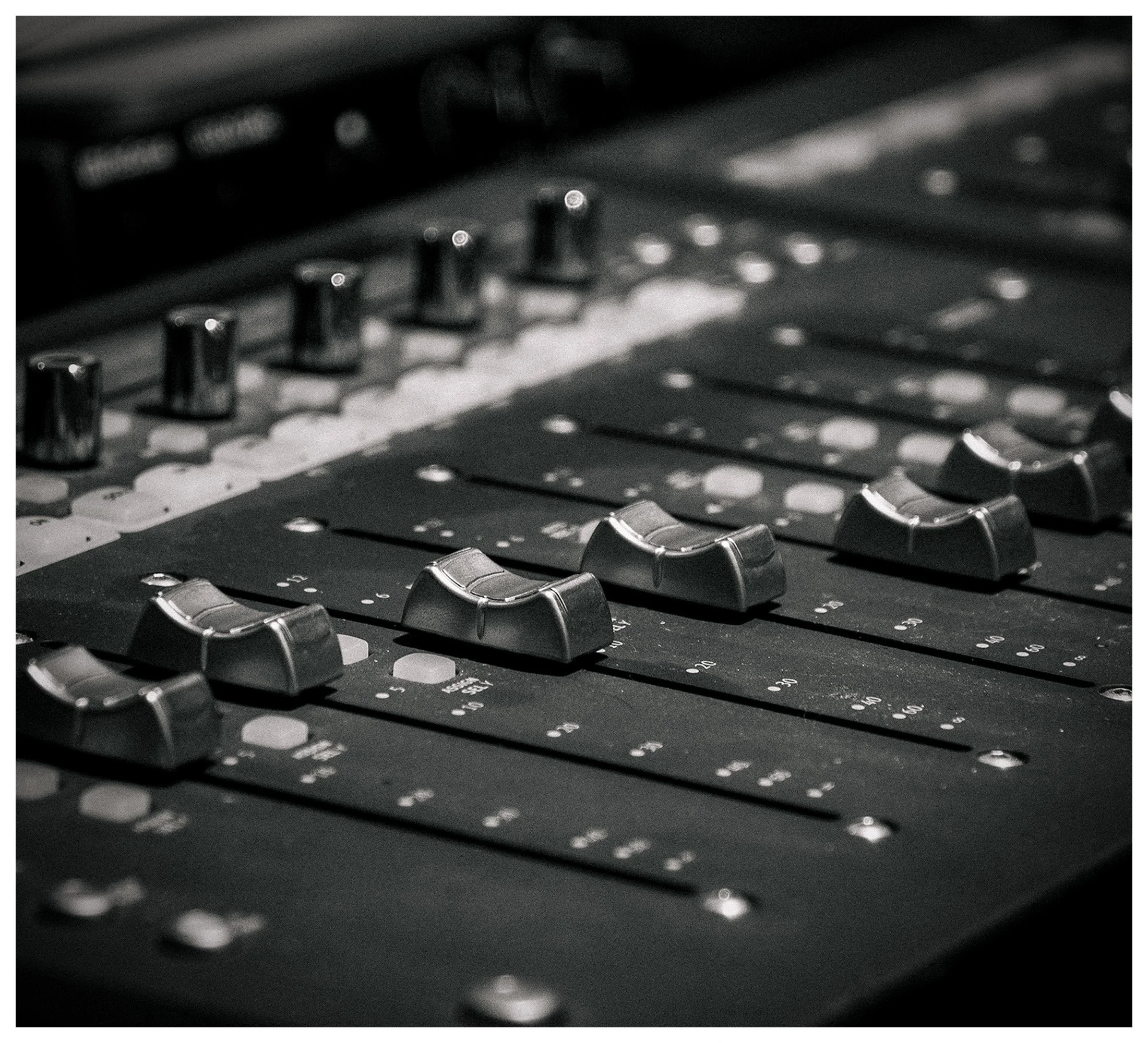 Close-up image of a black audio mixing console showing numerous sliders and knobs.