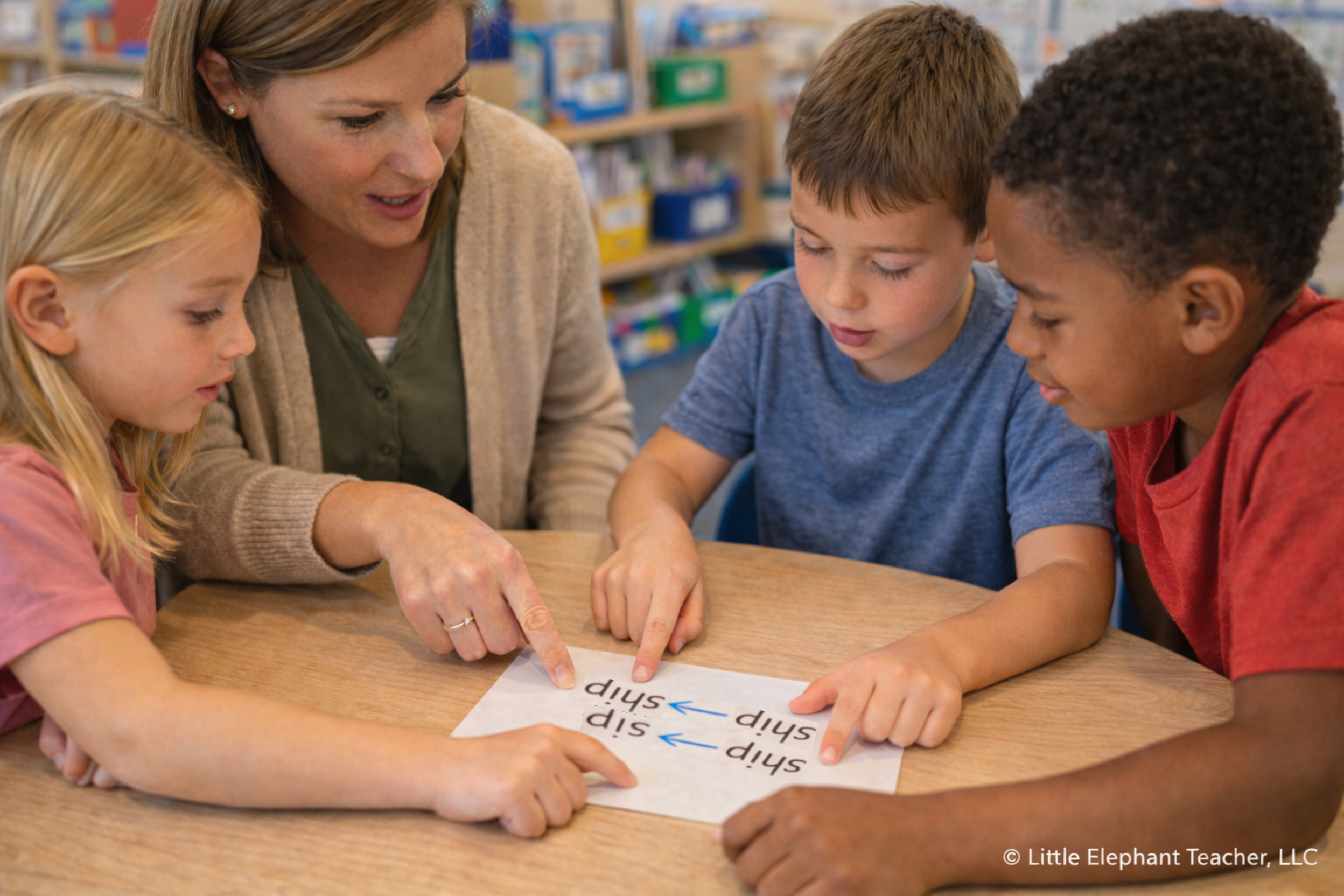 Teacher guiding a small group of elementary students during phonics instruction while students point to decoding error examples during reading practice.