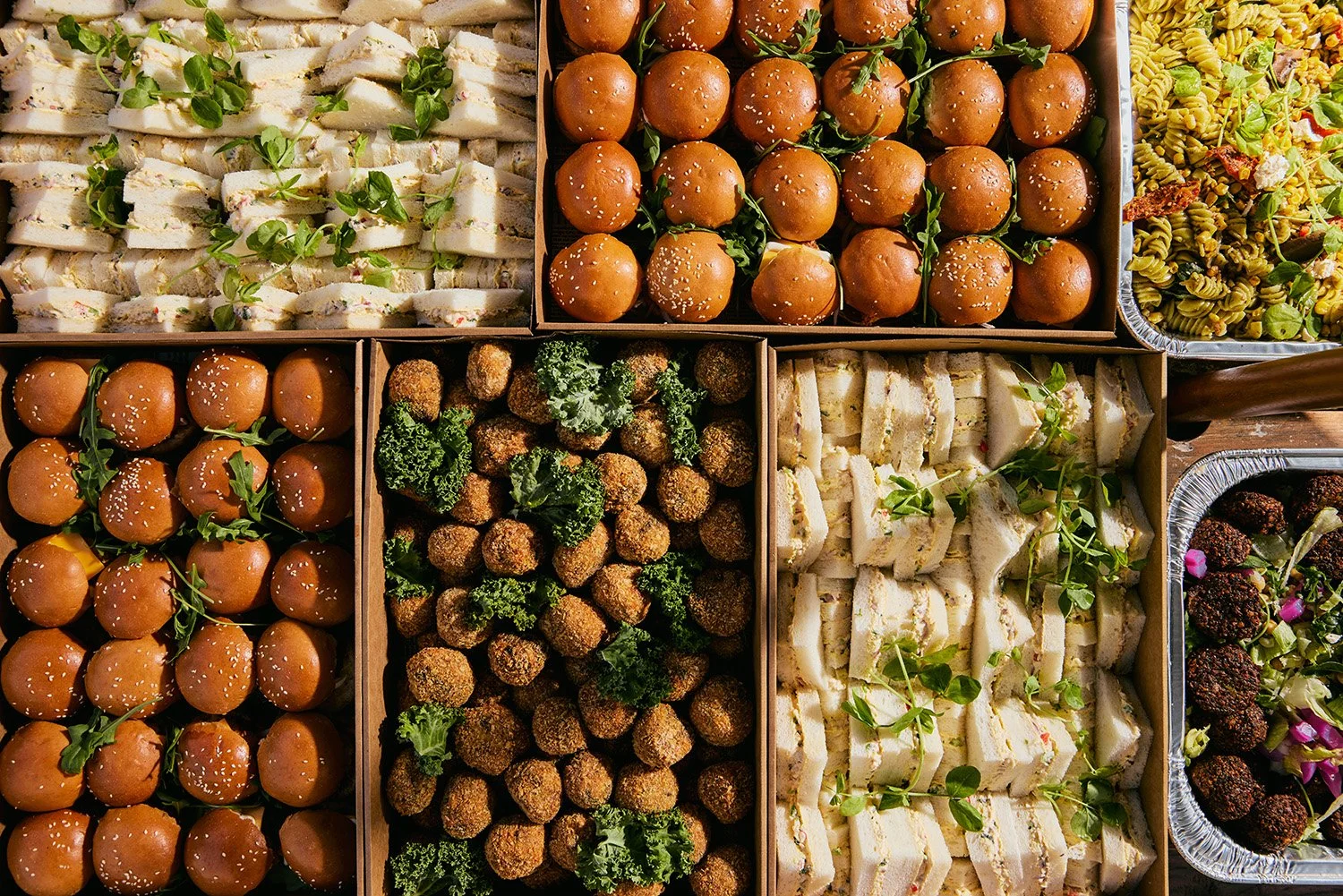 A tray of assorted sandwiches, croissants, and desserts on a wooden table, with condiment salt and pepper shakers, napkins, and a menu nearby.