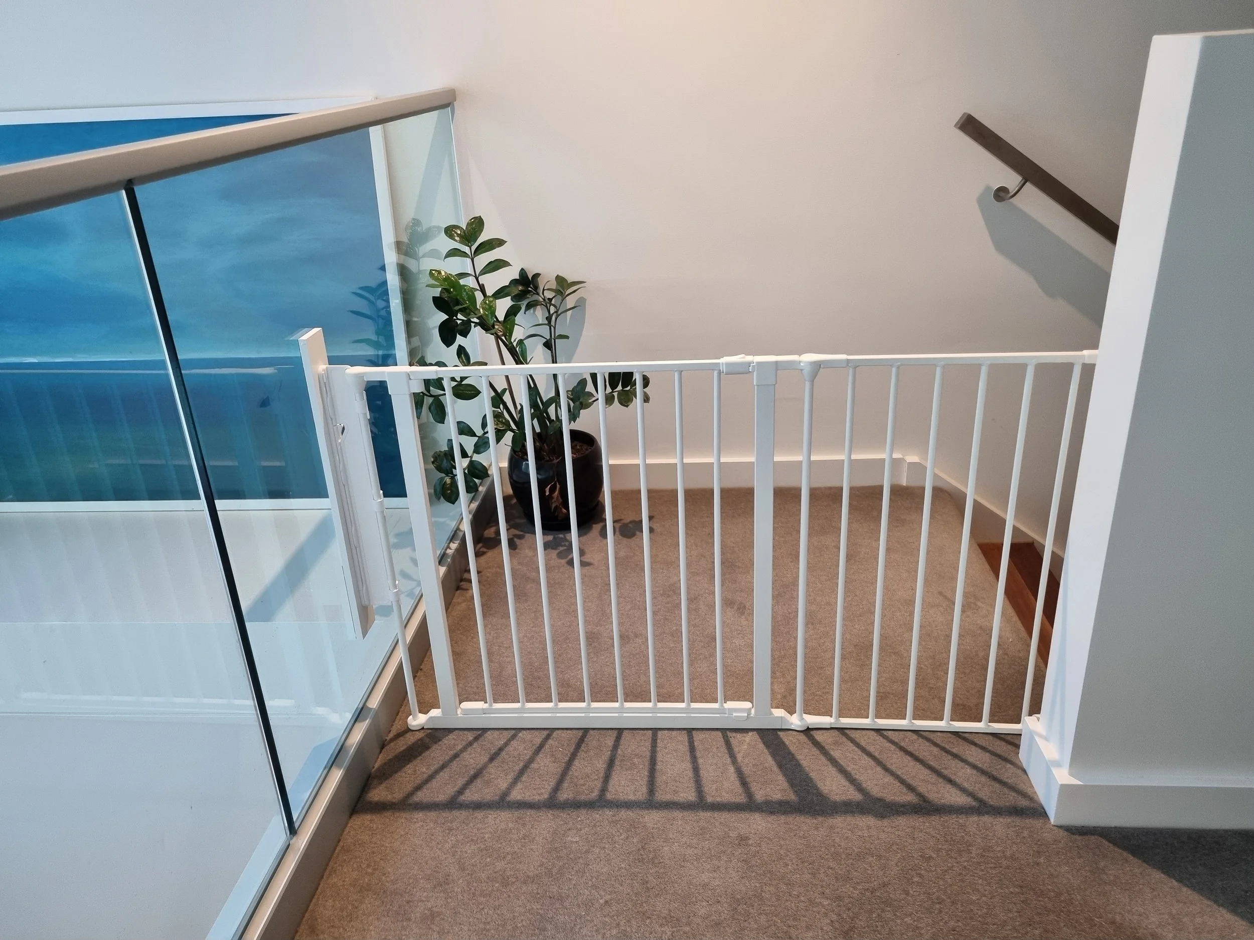 White baby gate at the top of stairs next to a glass balustrade