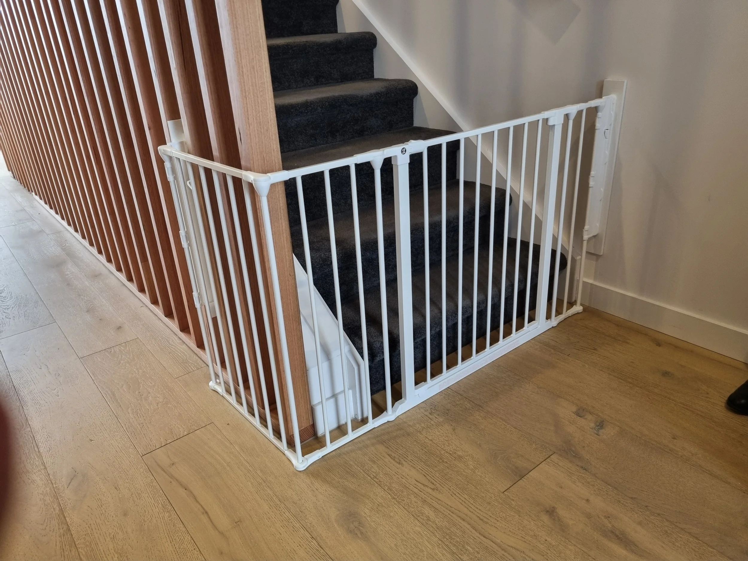 White angled baby gate at the bottom of carpeted stairs