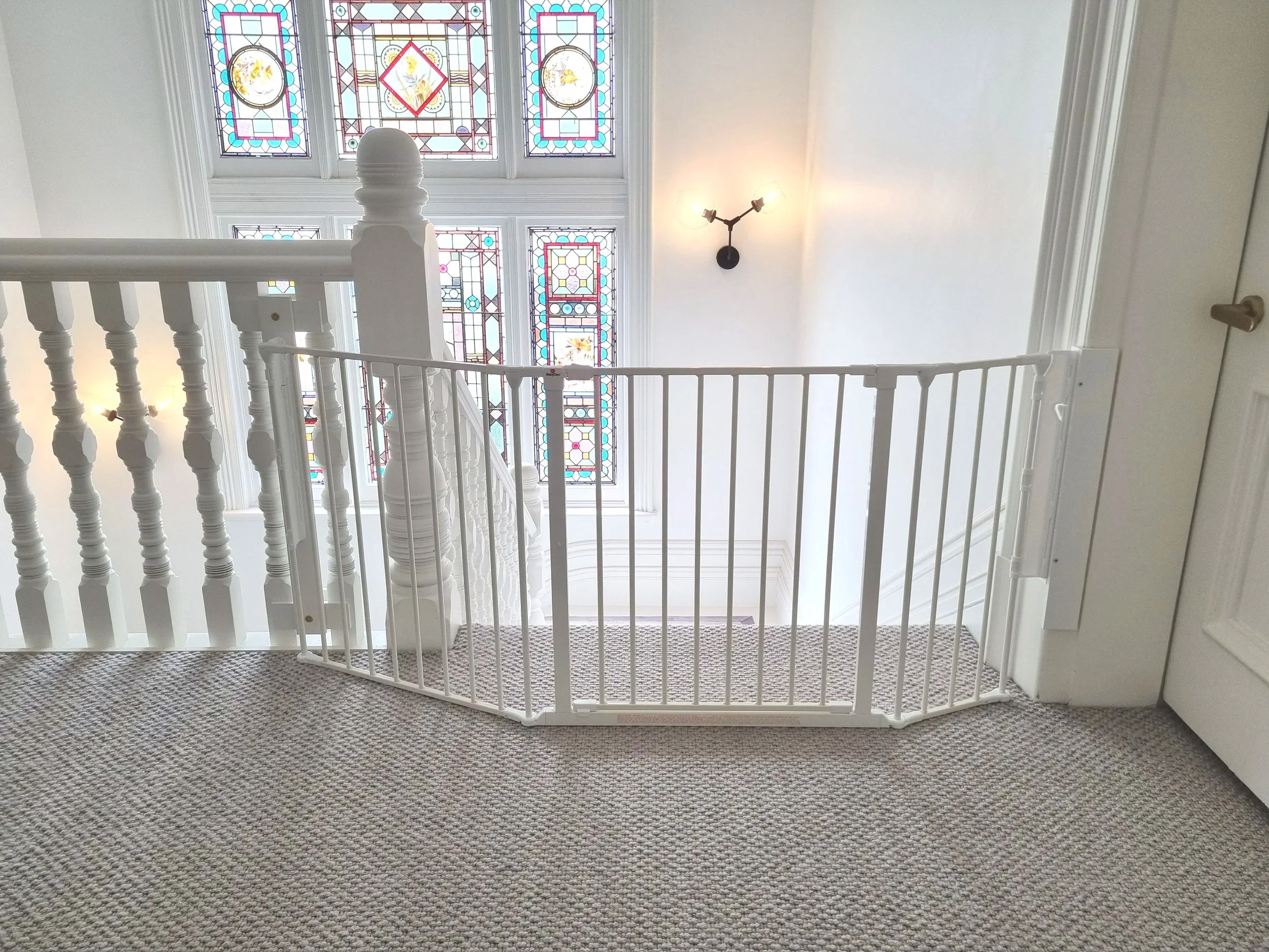 White angled baby gate at the top of stairs with a timber balustrade