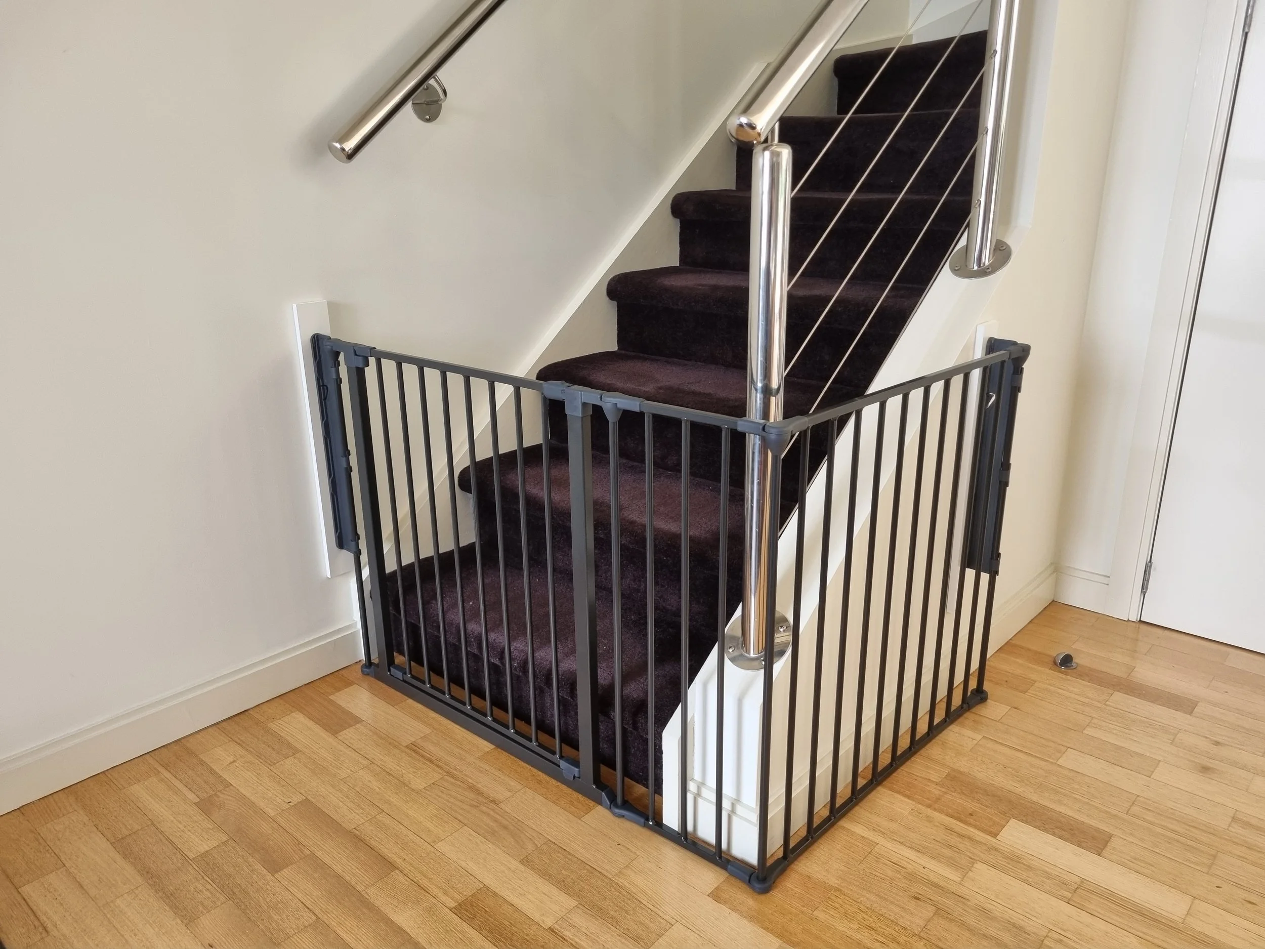 Black baby gate at the bottom of carpeted stairs beside a handrail