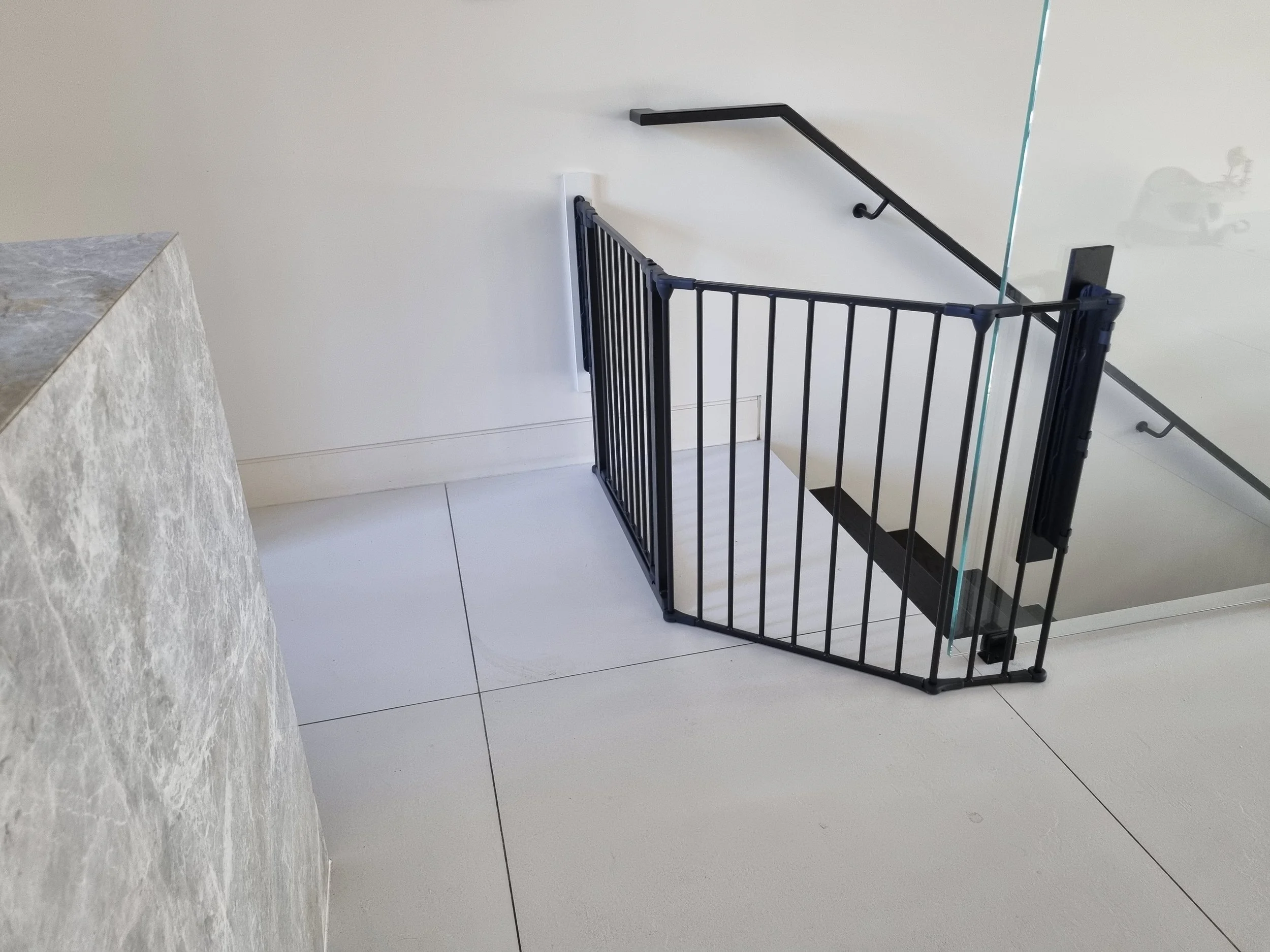 Black baby gate at the top of stairs on a tiled landing