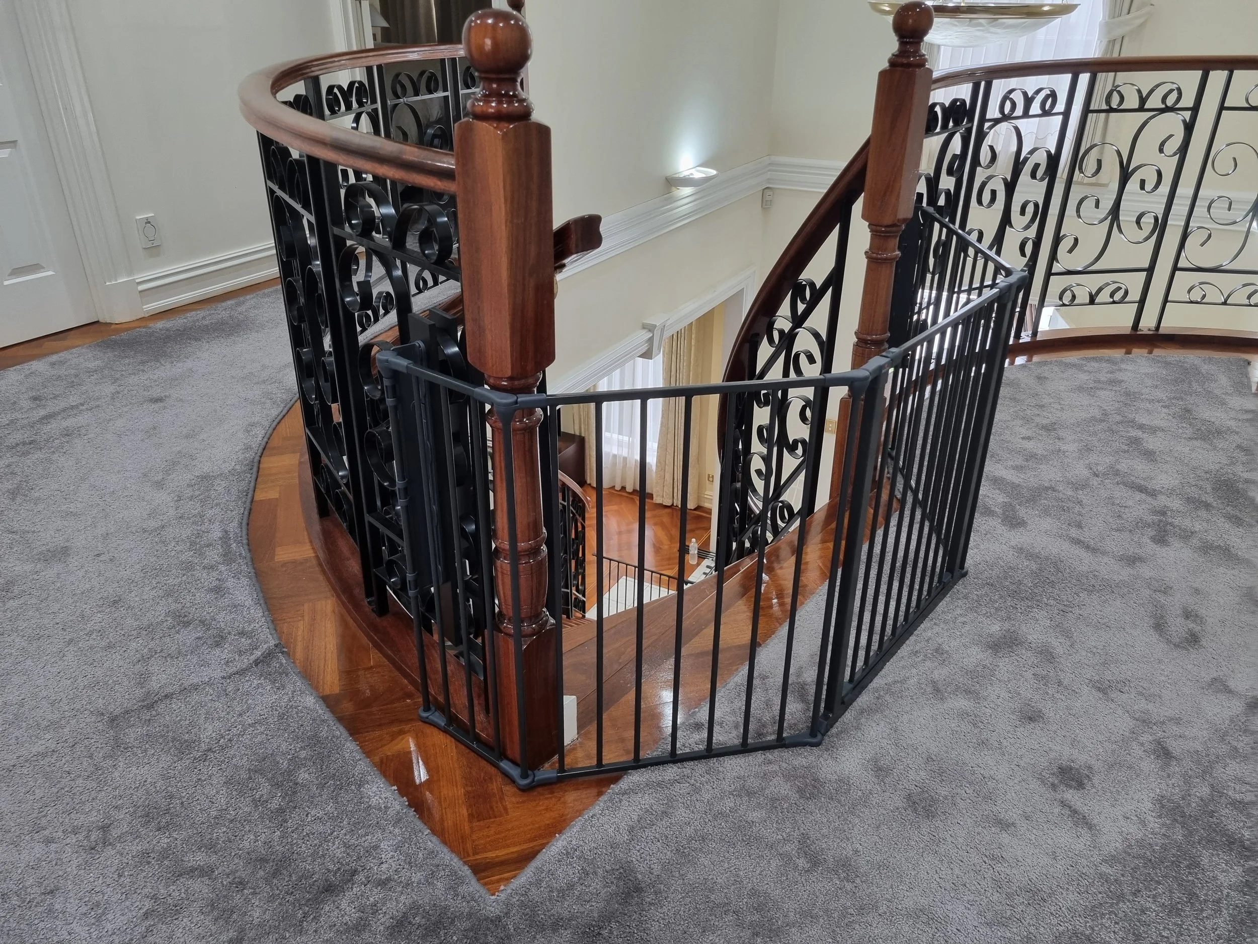 Black baby gate around the top of a spiral staircase with an iron balustrade