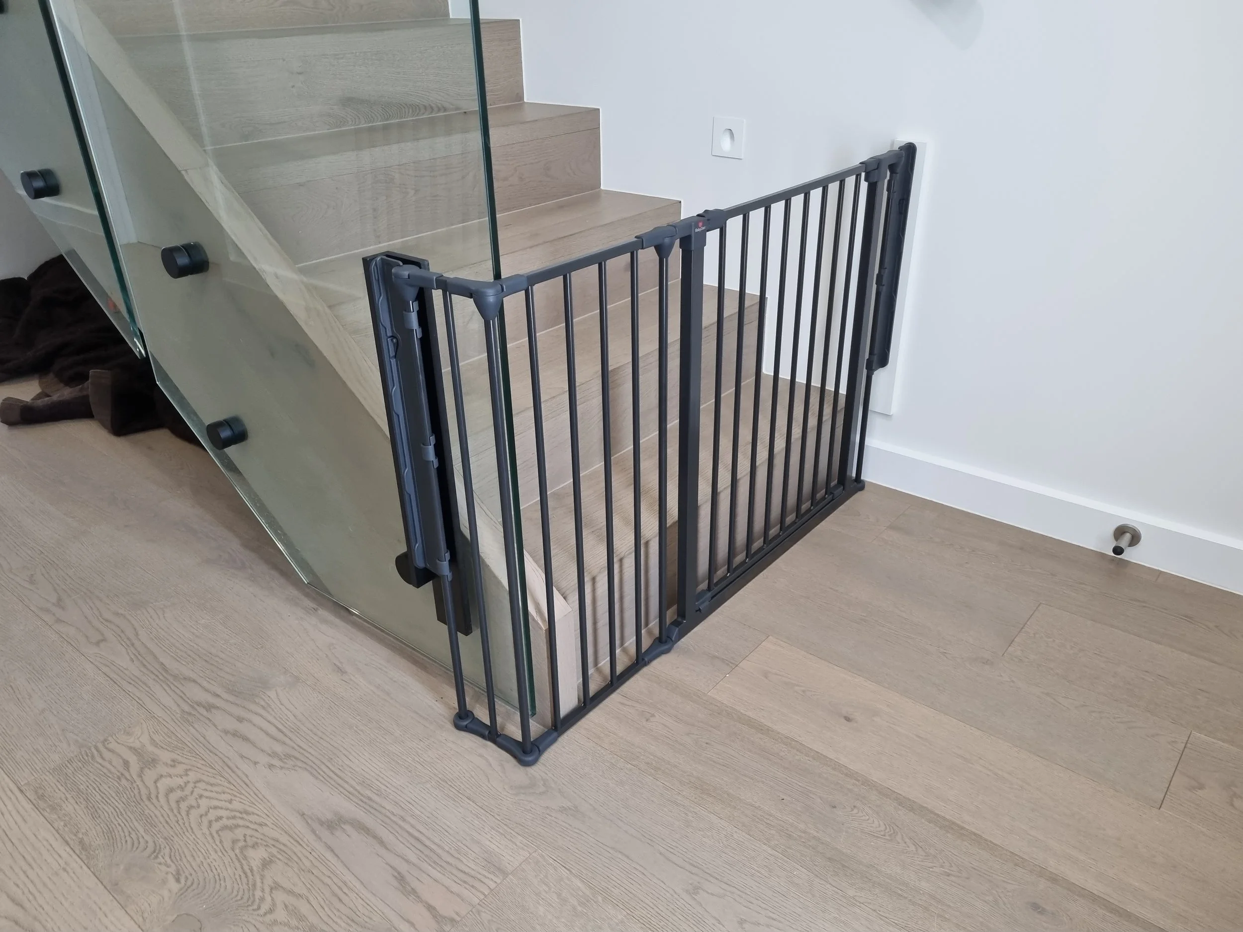 Black baby gate at the bottom of stairs beside a glass balustrade
