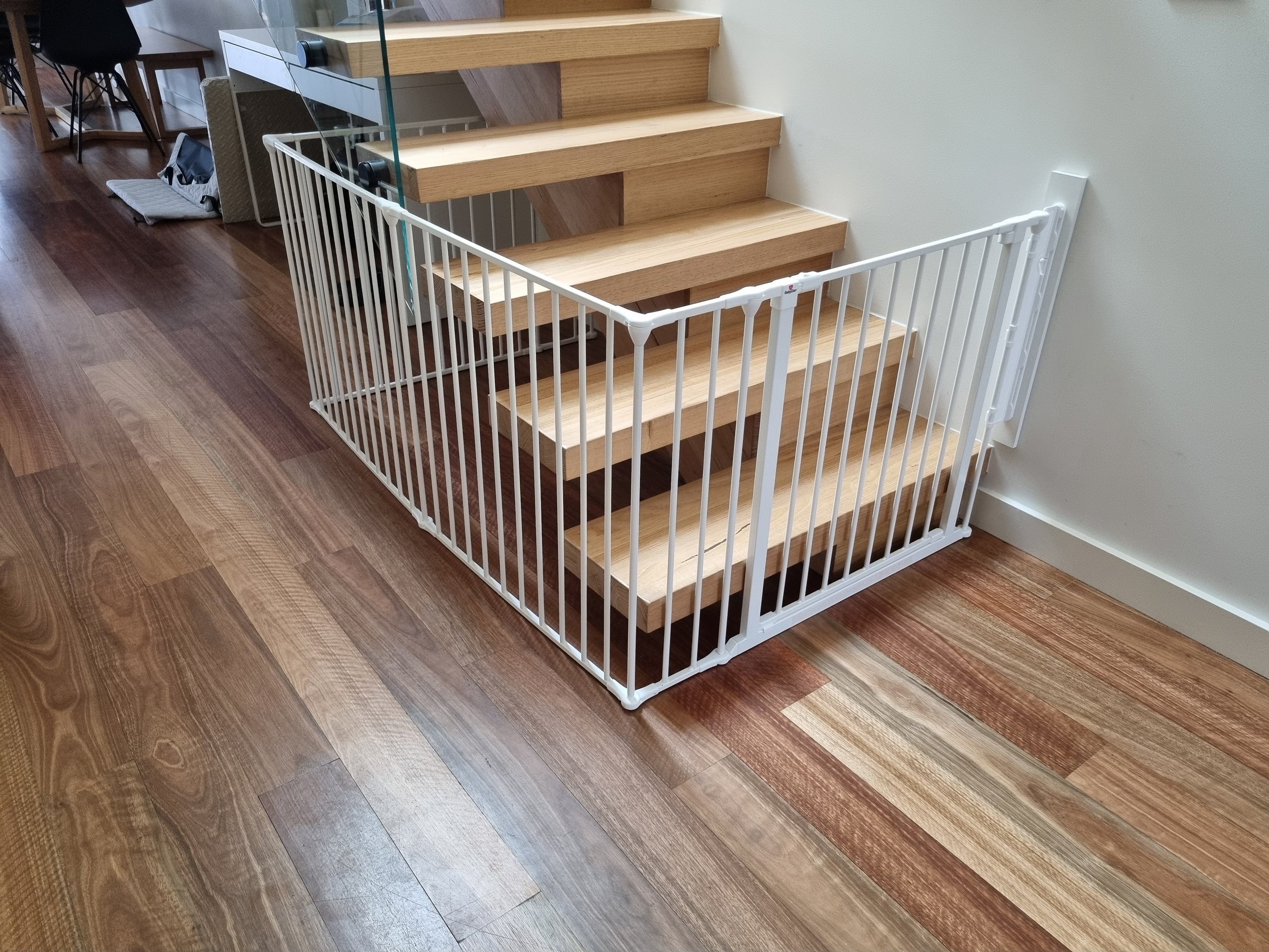 White wrap-around baby gate at the base of open timber stairs