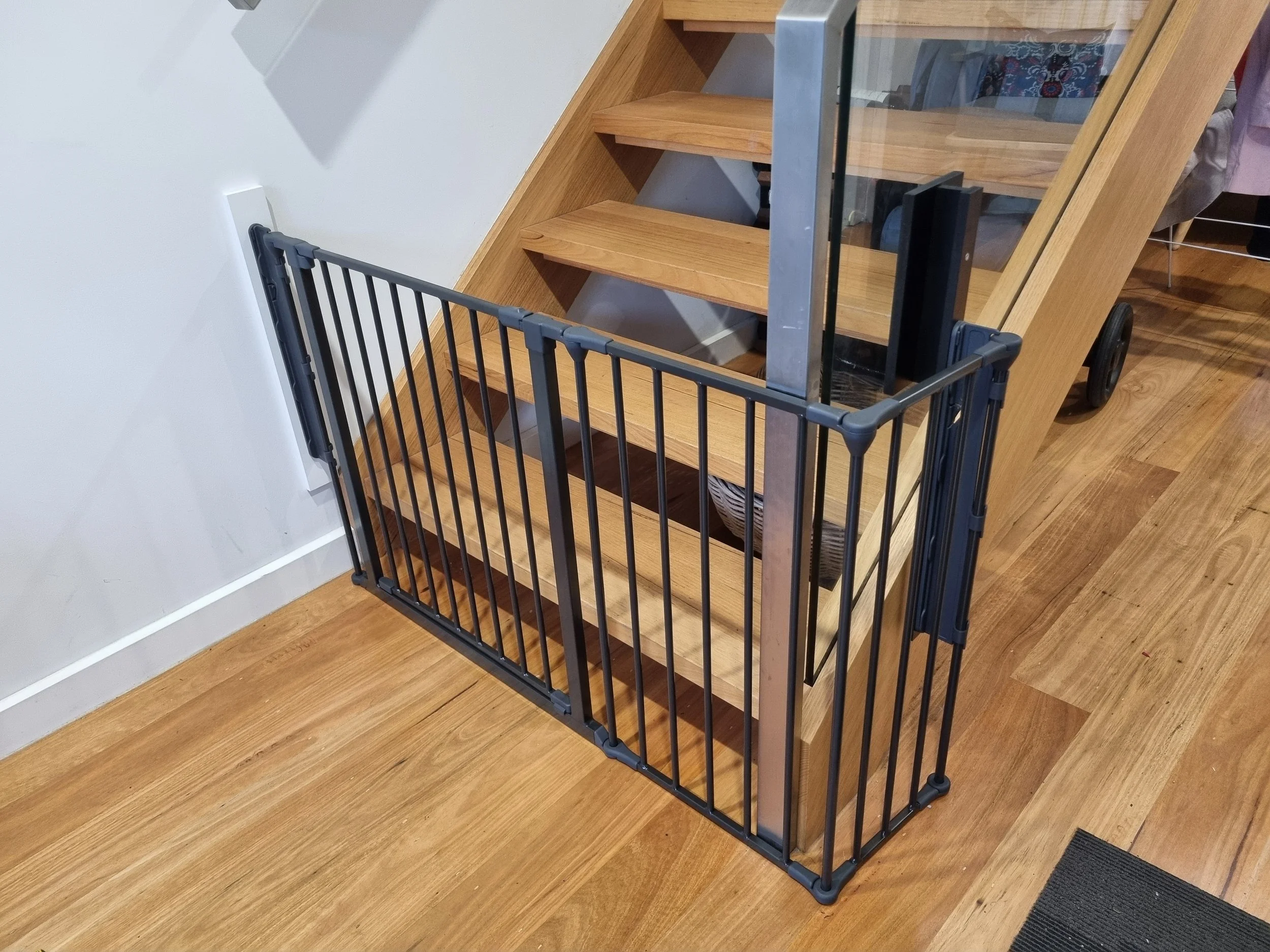 Black L-shaped baby gate around the base of open timber stairs