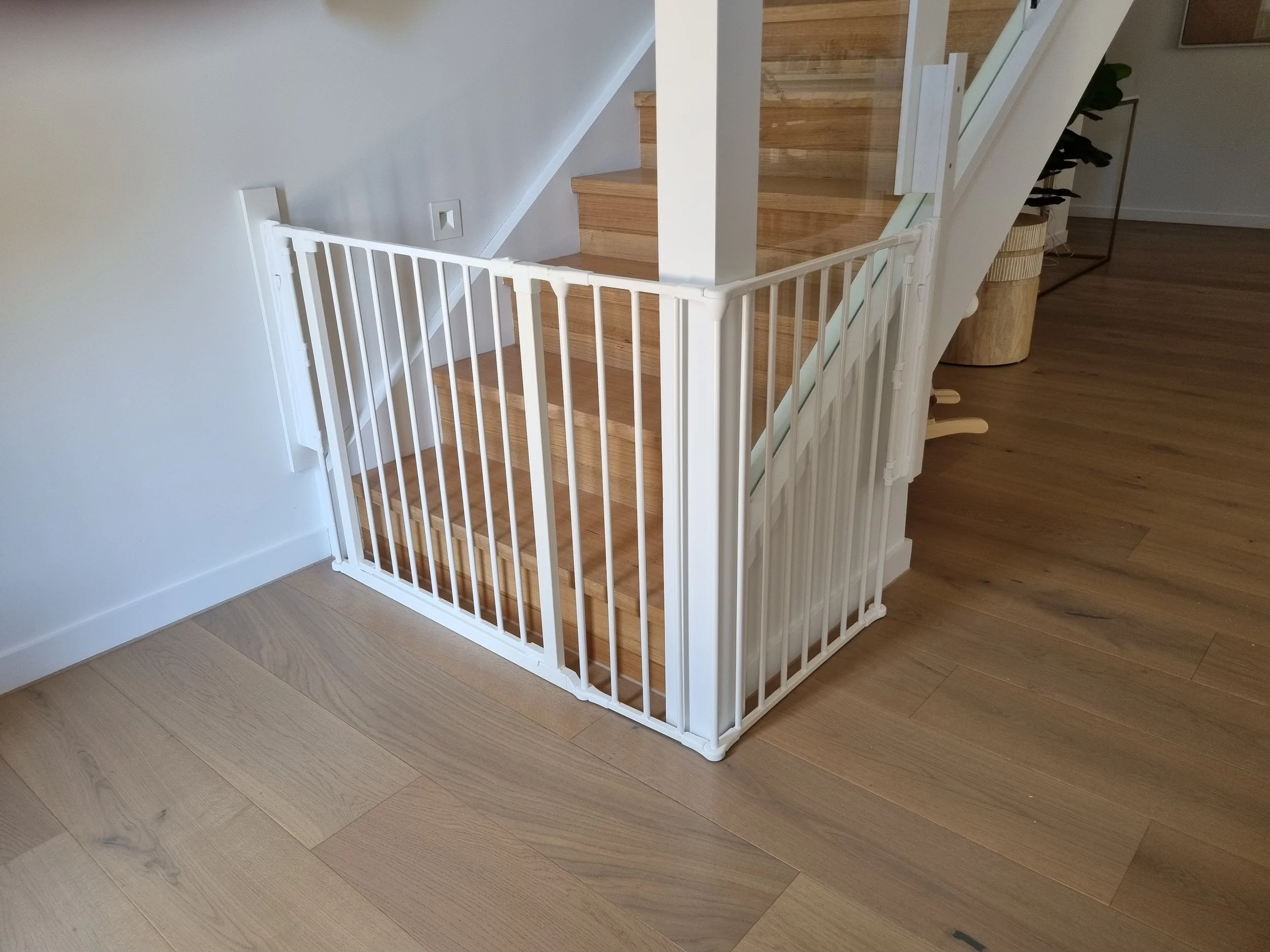 White angled baby gate at the bottom of timber stairs