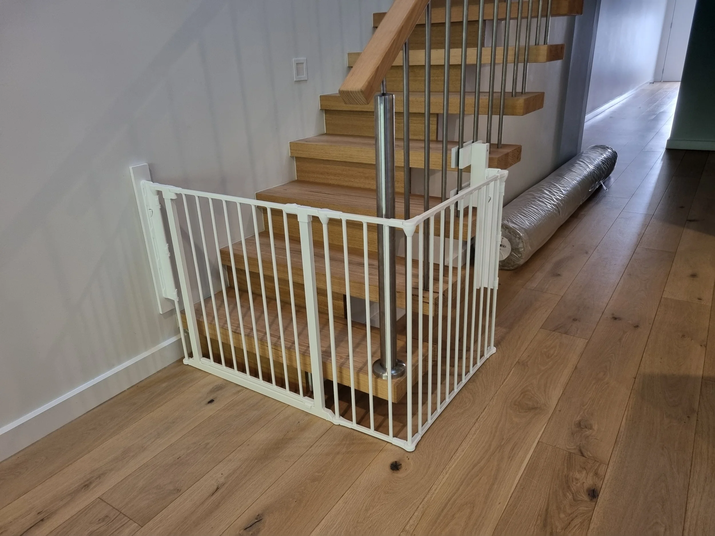 White baby gate around the base of open stairs with a steel balustrade