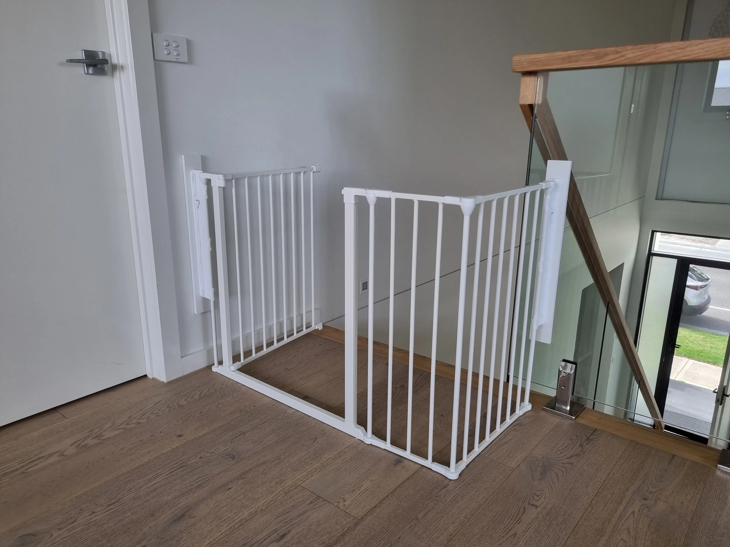 White L-shaped baby gate at the top of stairs beside a timber handrail