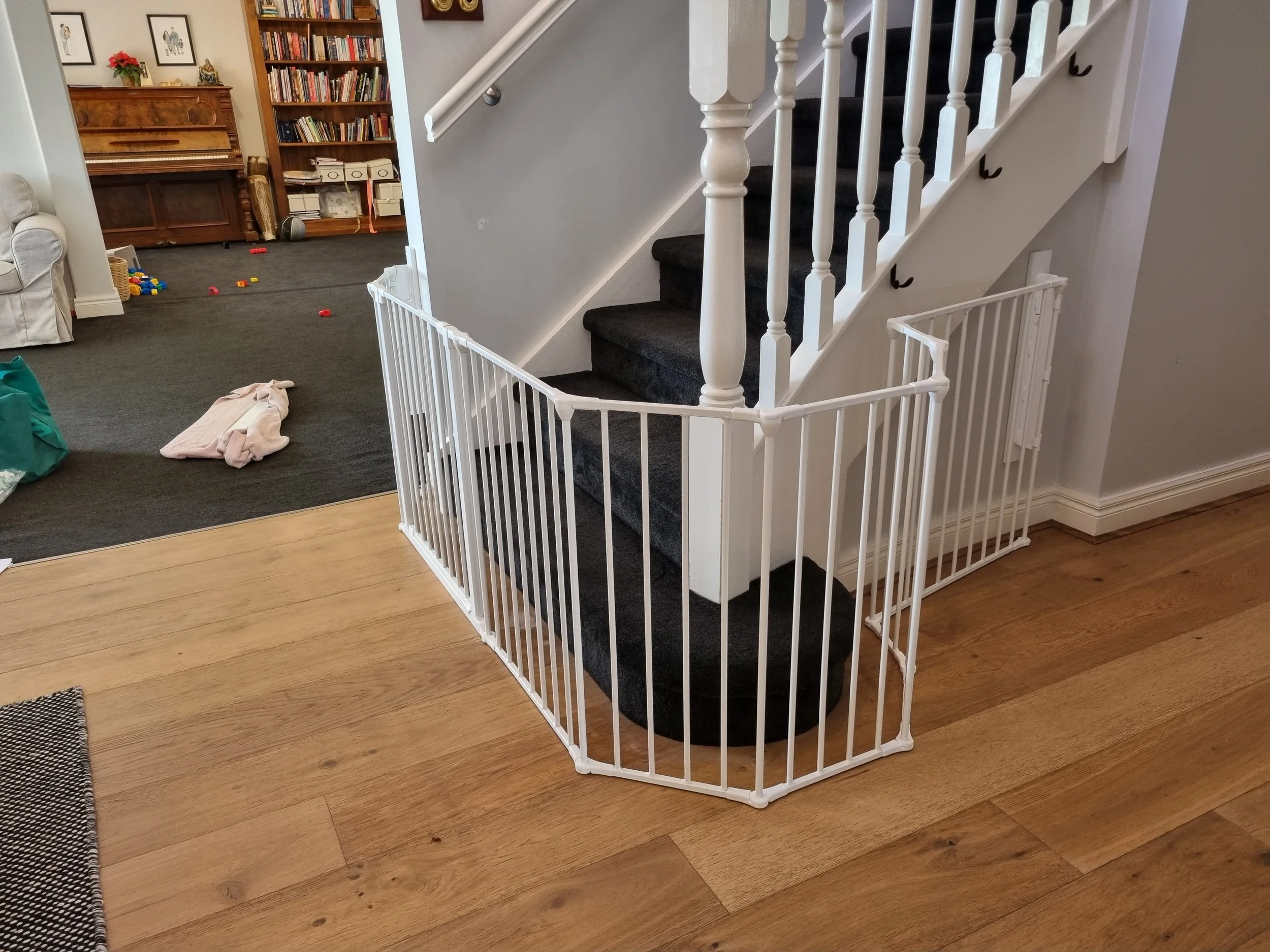 White multi-angle baby gate around the base of stairs with a white balustrade