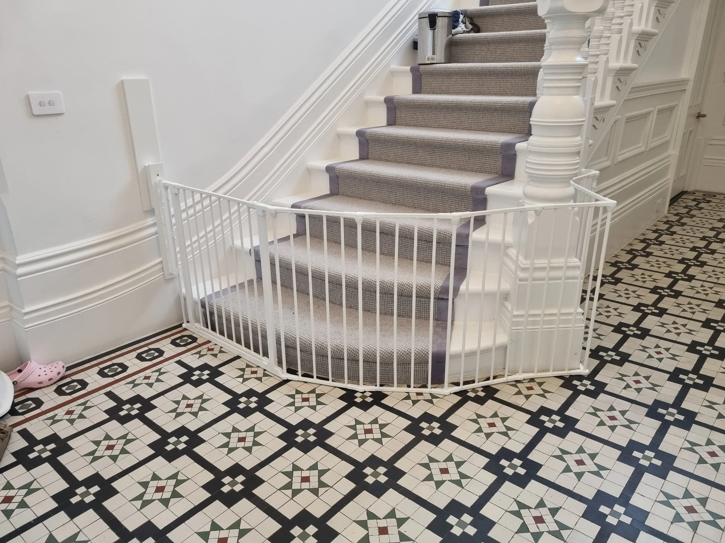 White curved baby gate around the base of a carpeted staircase