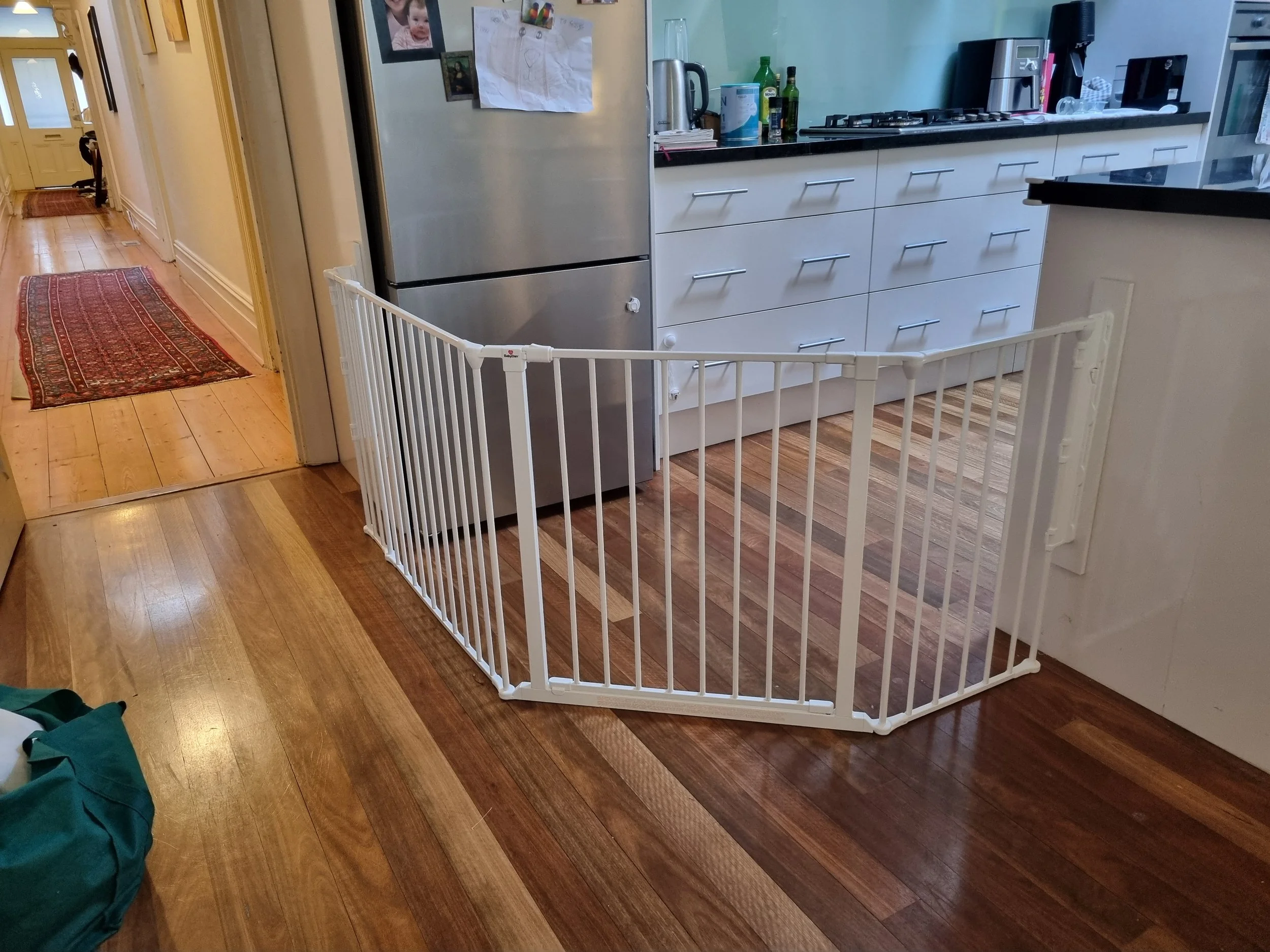 White multi-angle baby gate closing off a kitchen on a timber floor
