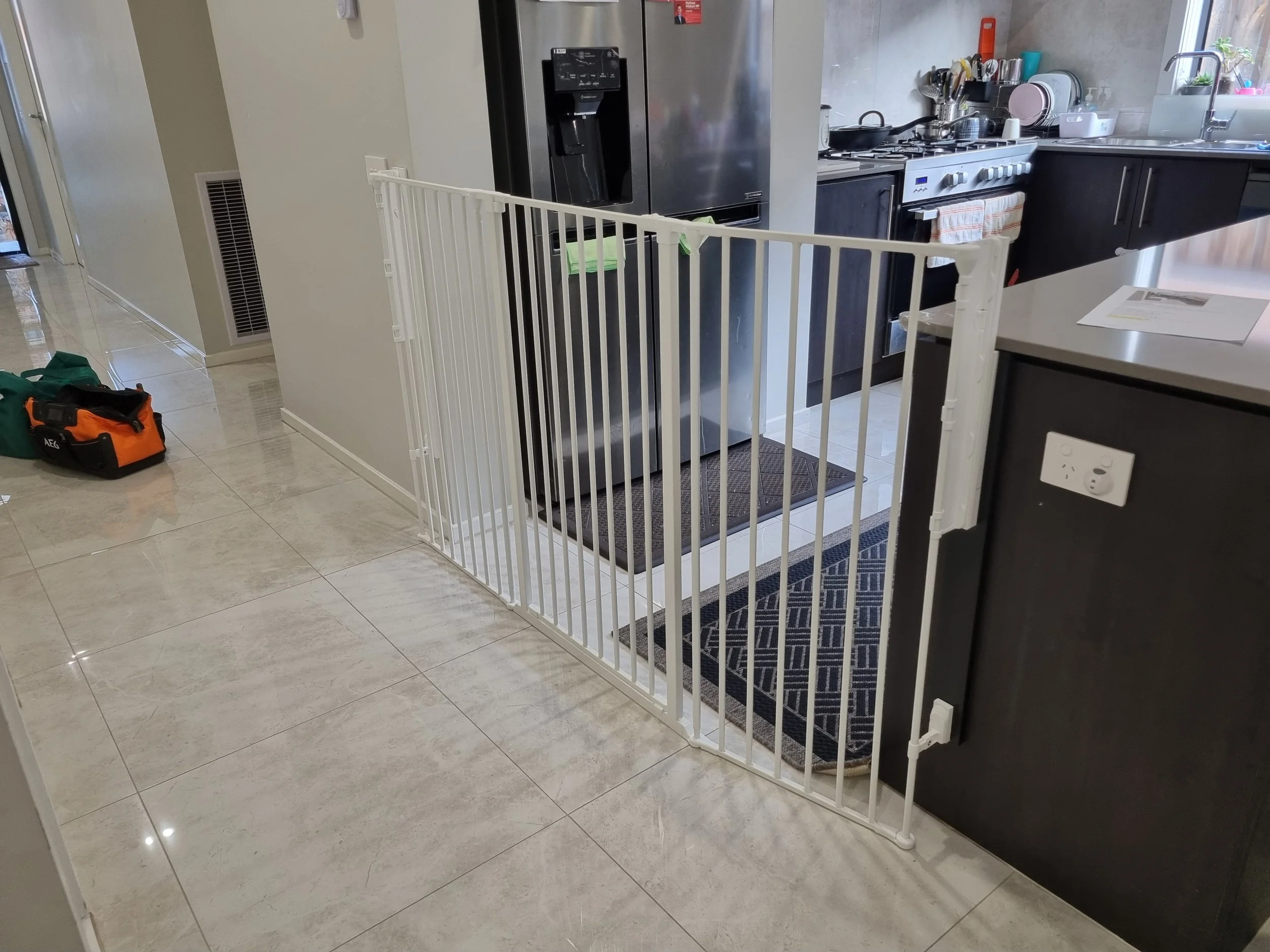 White baby gate at the entrance to a kitchen with dark cabinets