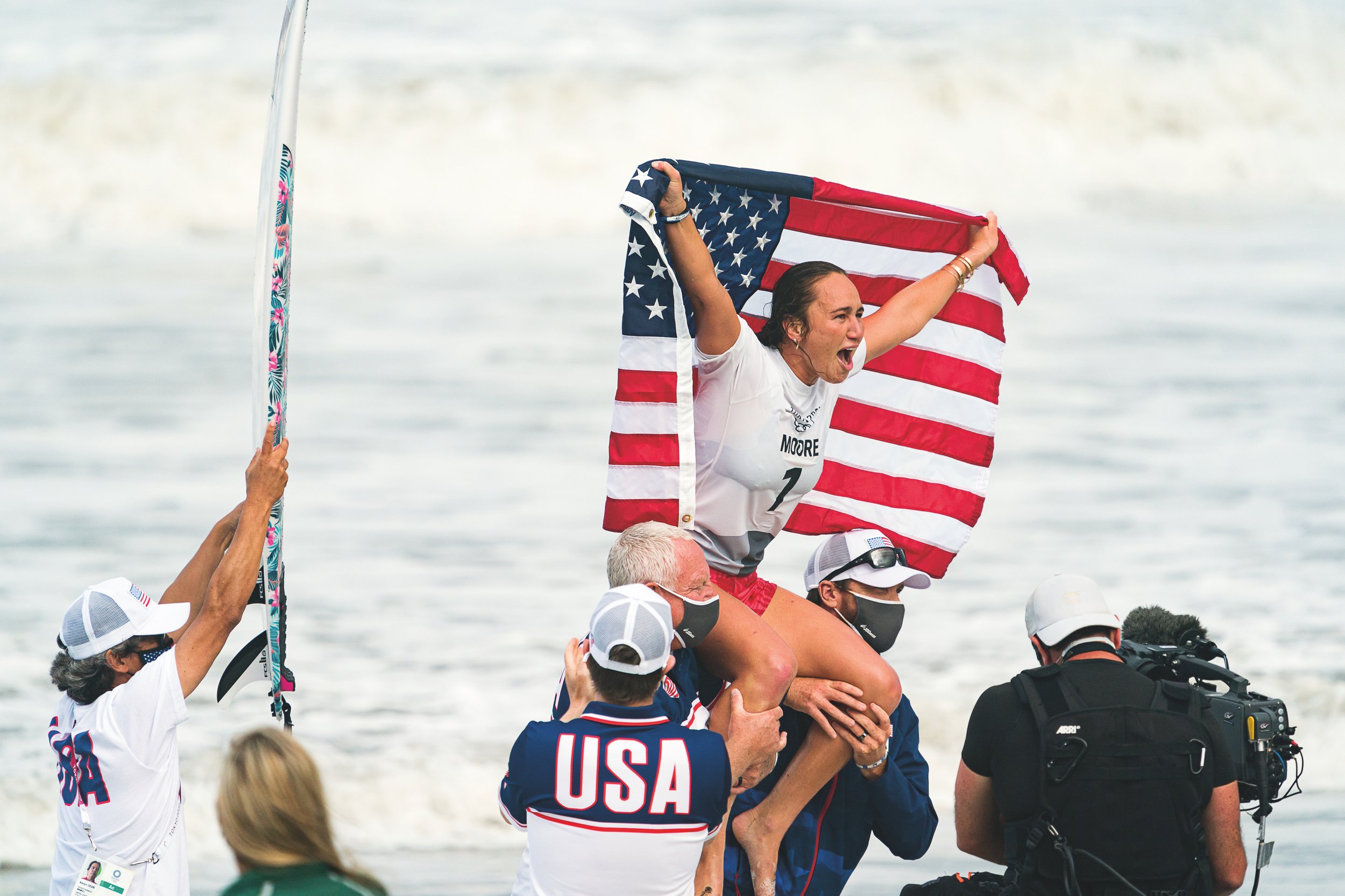  Moore is carried off the beach after her historic win at the Tokyo 2020 Summer Olympics. (Photo by Ben Reed, courtesy International Surfing Association.) 