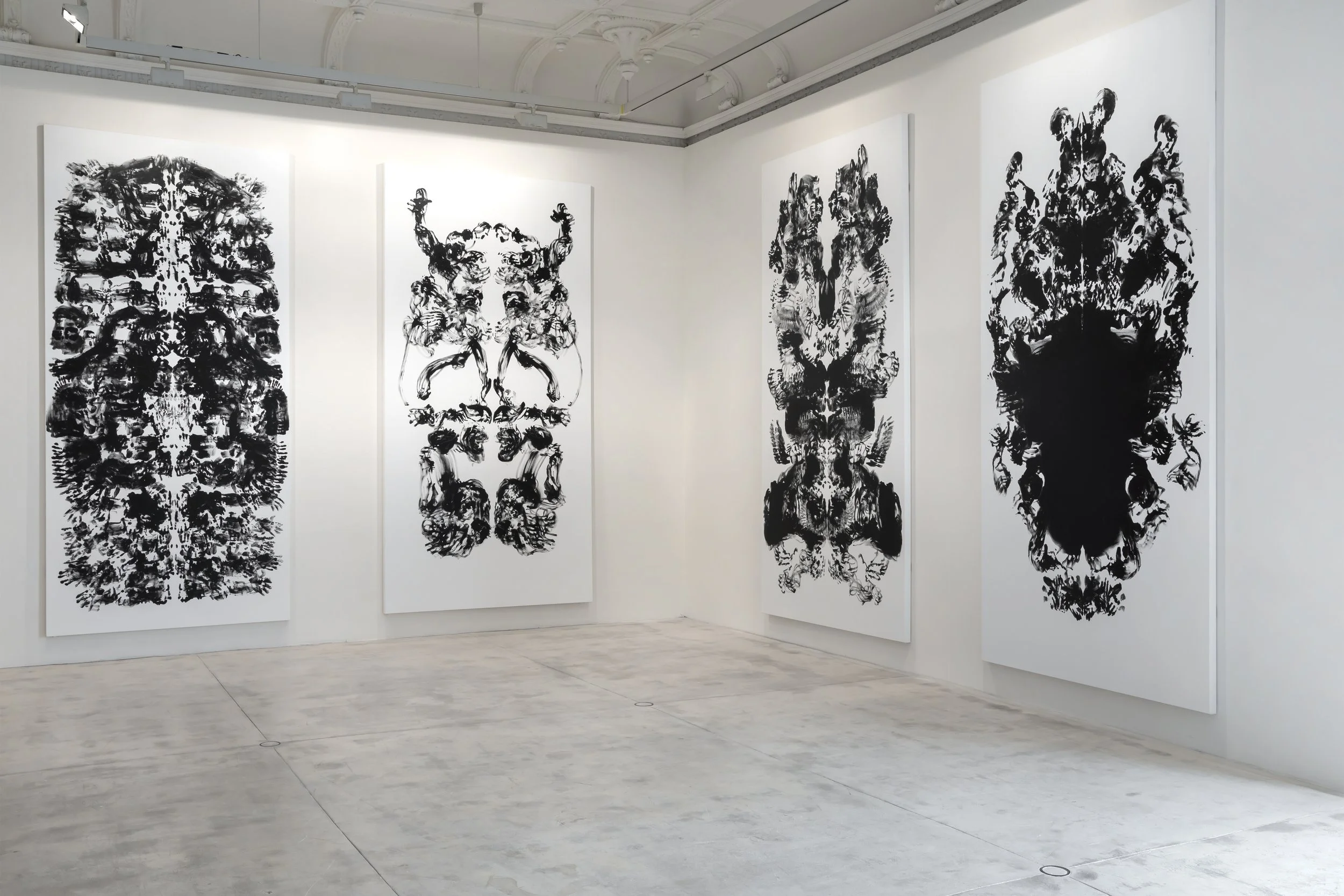 Gallery of five large black and white abstract symmetrical paintings on white walls in an art gallery with concrete floors.