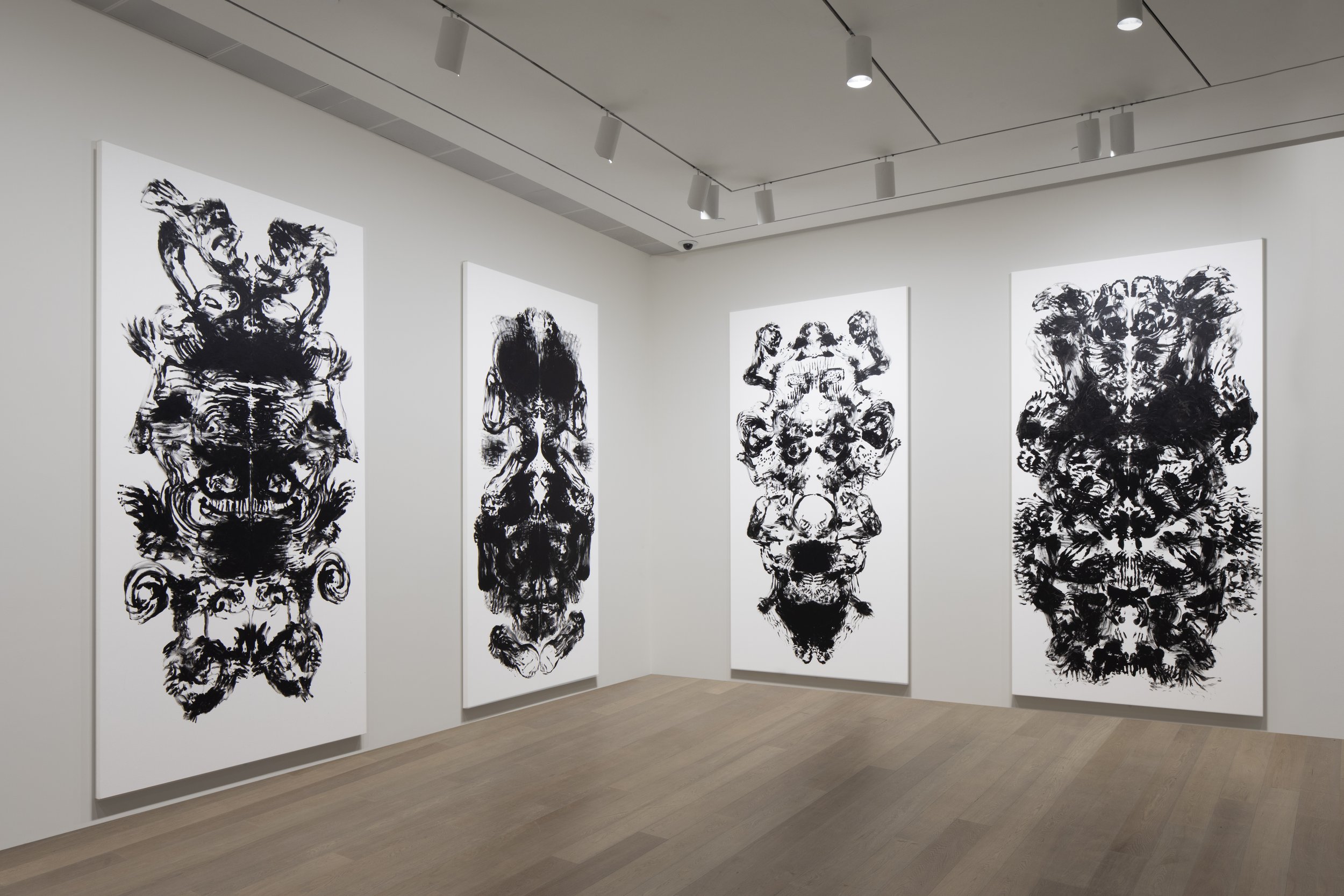 Art gallery with four large black and white abstract ink paintings on white walls, illuminated by track lighting, wooden flooring, in a minimalist setting.