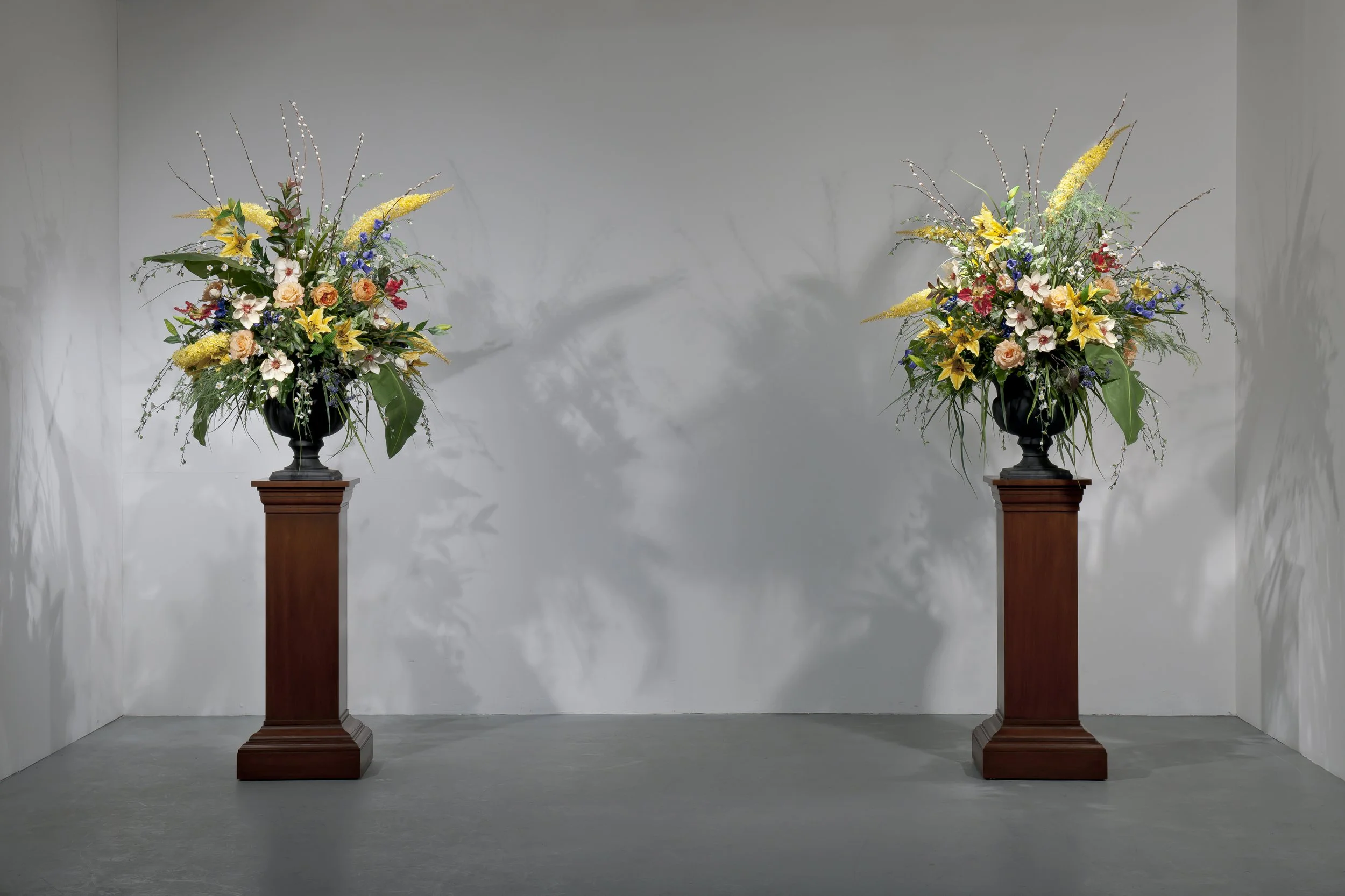 Mark Wallinger’s Double Still Life, 2009, consists of two identical displays of silk flowers: roses, lilies and other imperishable blooms arranged in plastic urns set against a plain wall background in a gallery space.