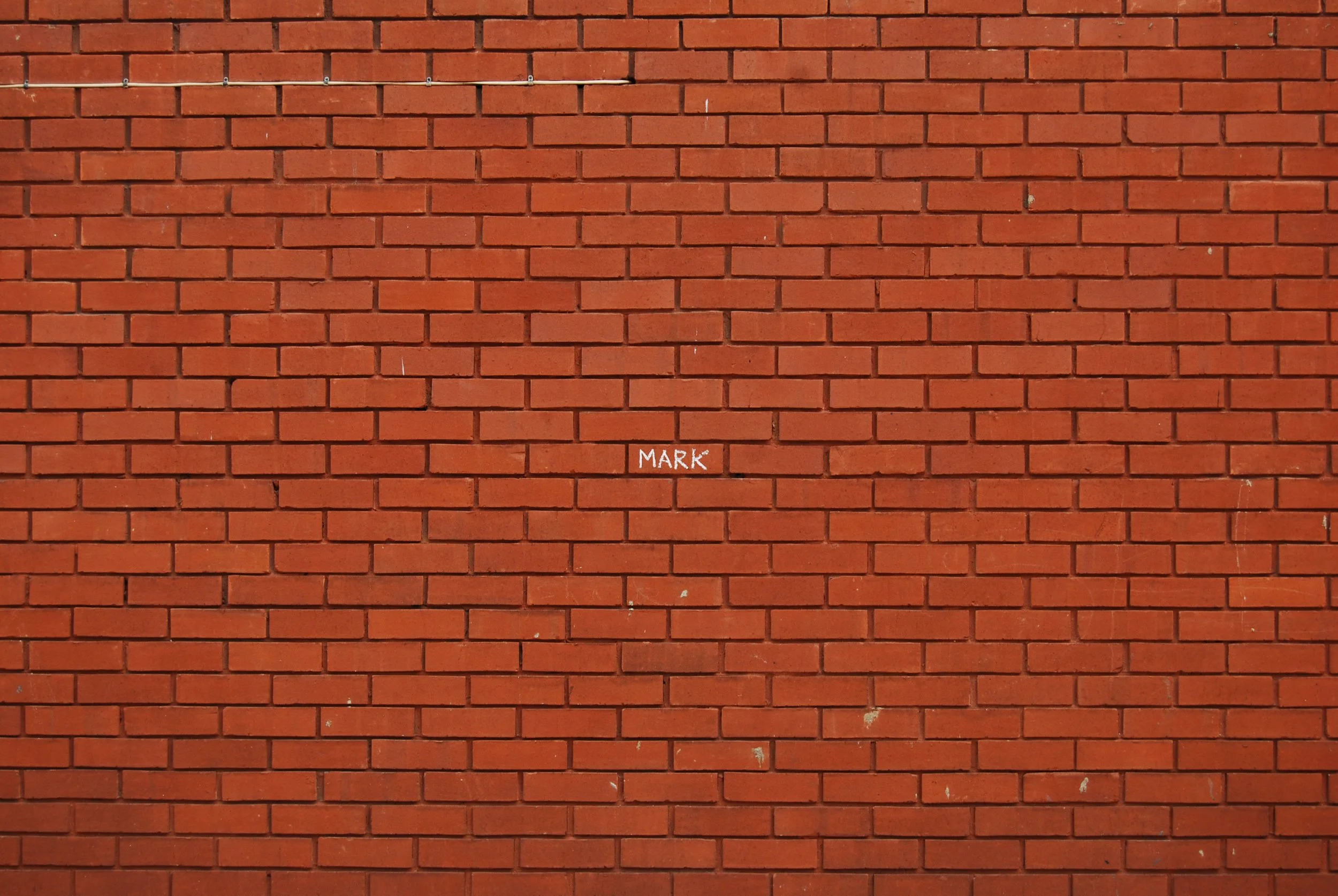 Red brick wall with a small white sign saying 'MARK' in the center.