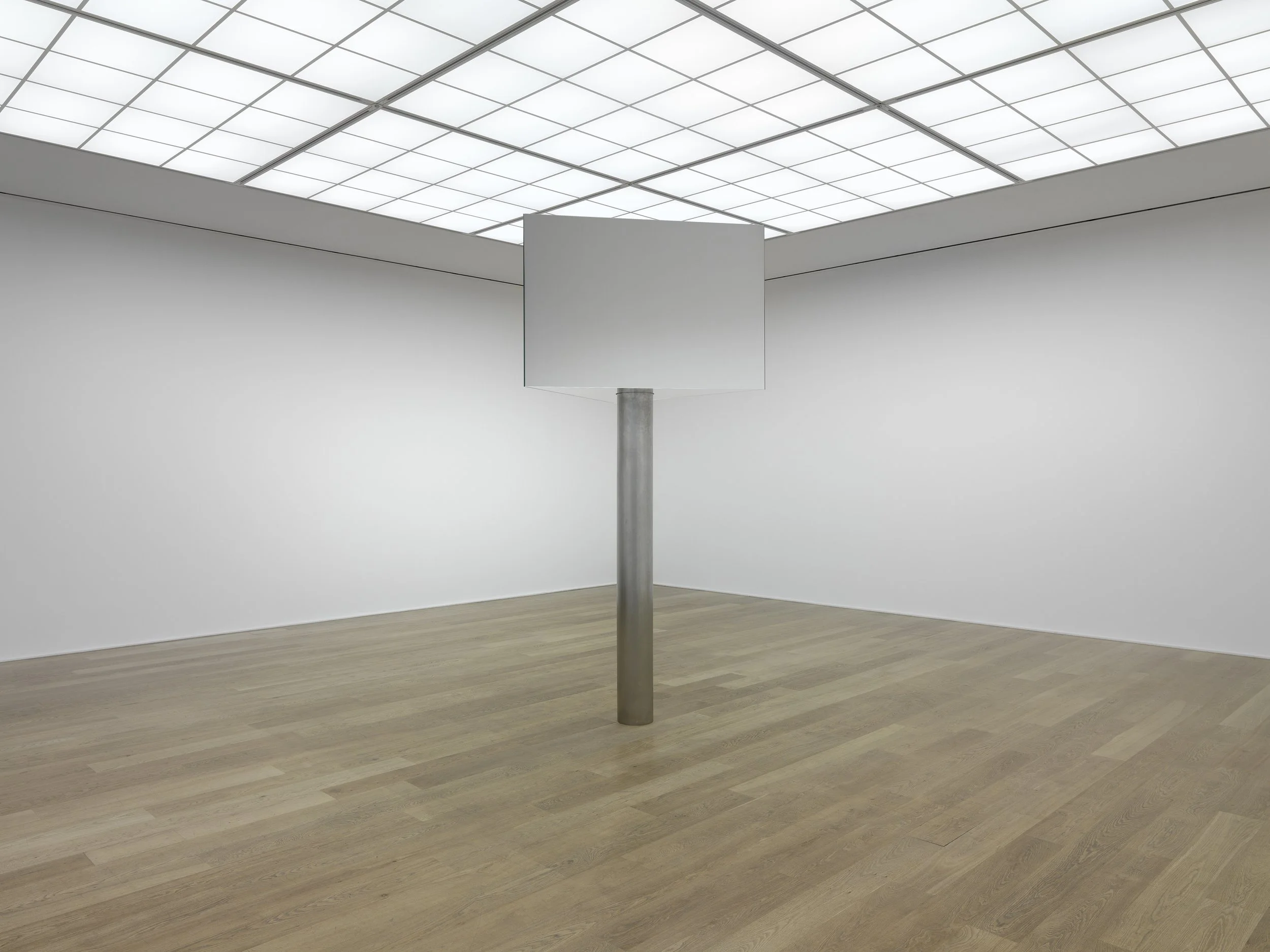 In a spacious gallery, Mark Wallinger’s Superego (2016) stands alone. This mirrored sculpture, inspired by the revolving New Scotland Yard sign, evokes authority and vigilance, reflecting viewers while remaining distant above them.