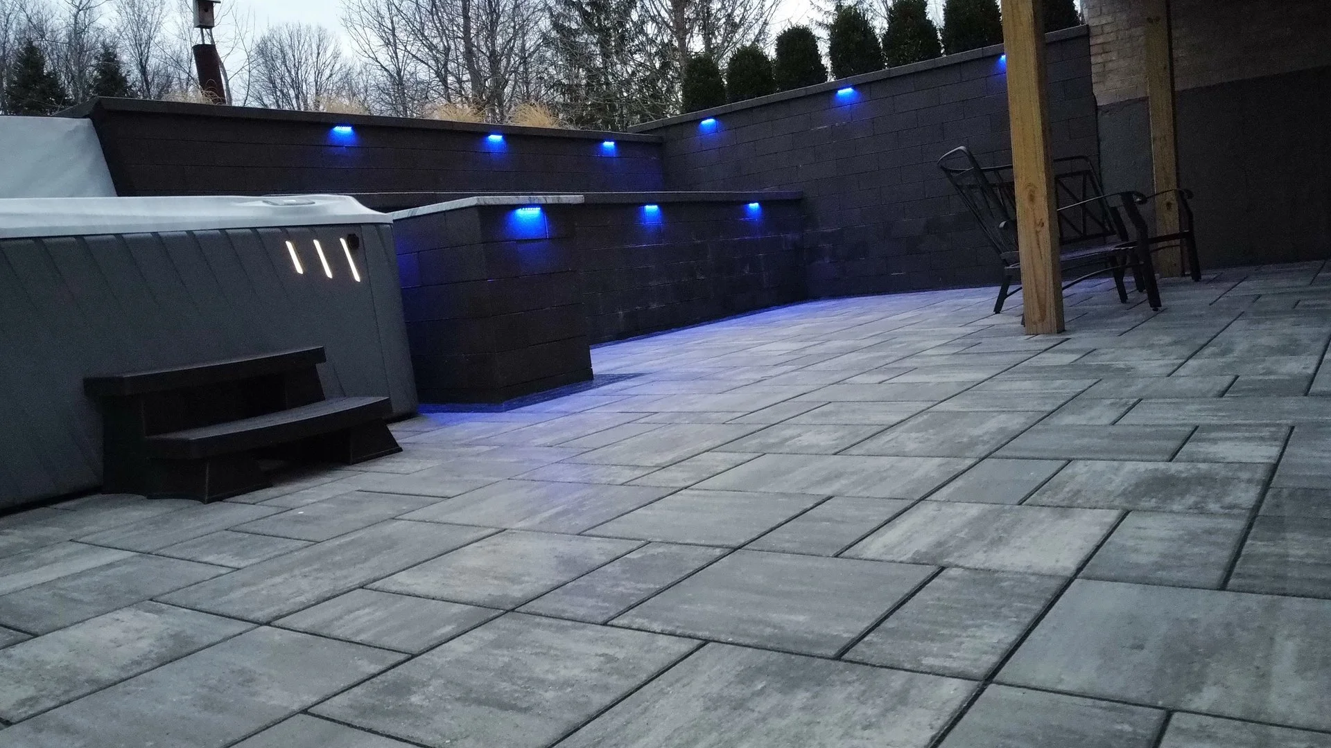 Slab paver patio leading to retaining walls with blue cap lights at dusk — Premier Landscaping