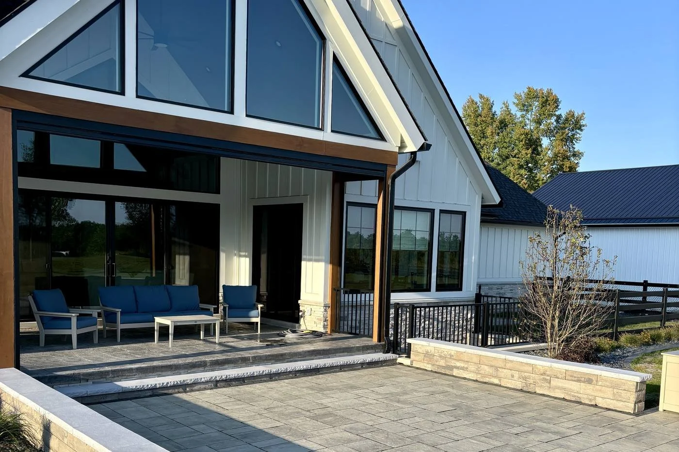 Covered porch with blue lounge seating opening onto a gray paver patio with seat walls — Premier Landscaping